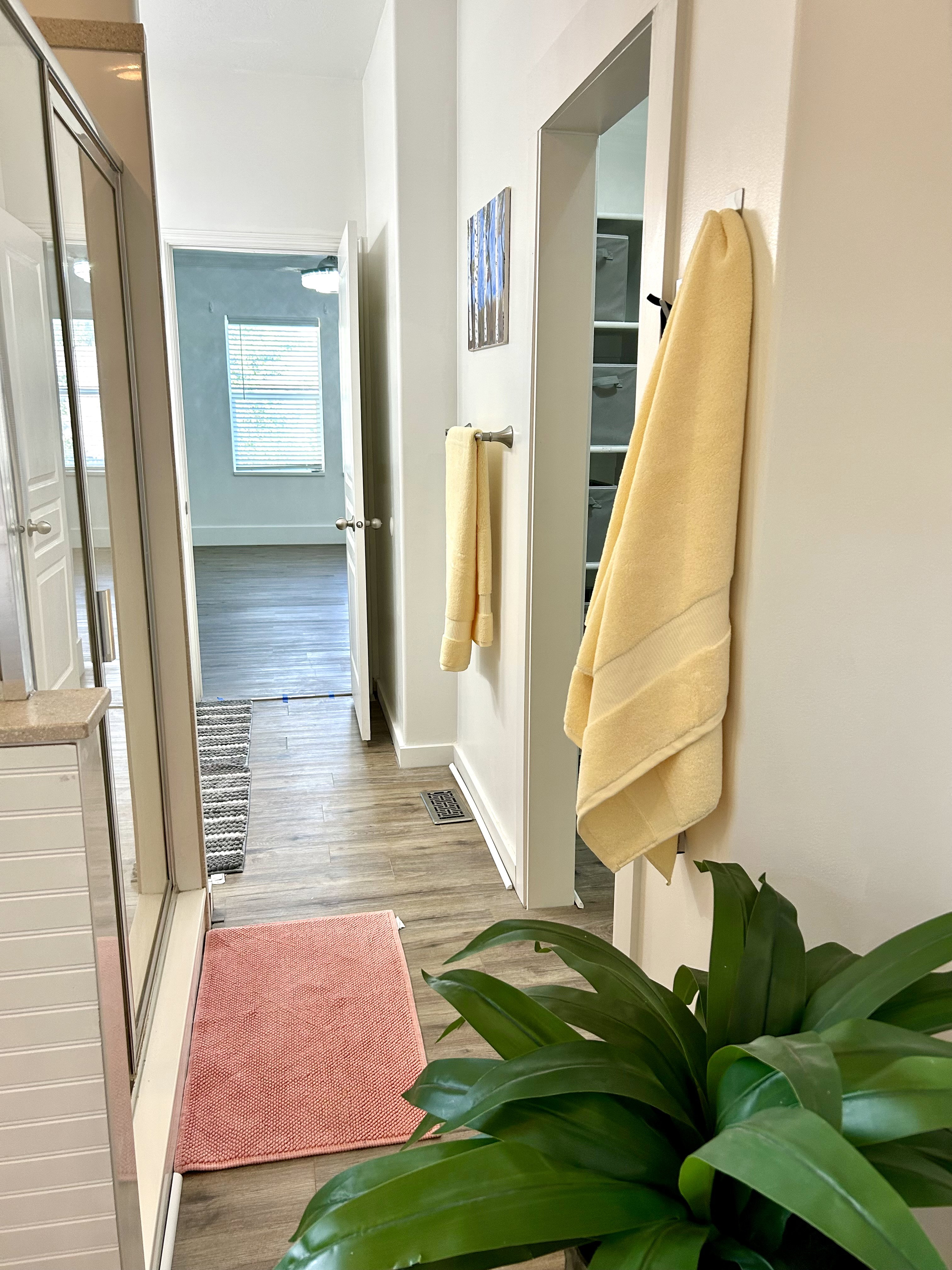 Wood-finish flooring throughout, featuring a shower enclosure with clear glass, a white shiplap vanity base, and an open doorway revealing built-in shelving