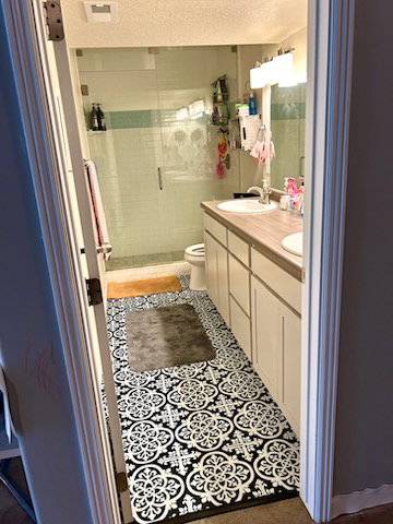 Full bathroom featuring a glass-enclosed shower, dual vanity with undermount sinks, wood-finish countertop, and patterned floor tile