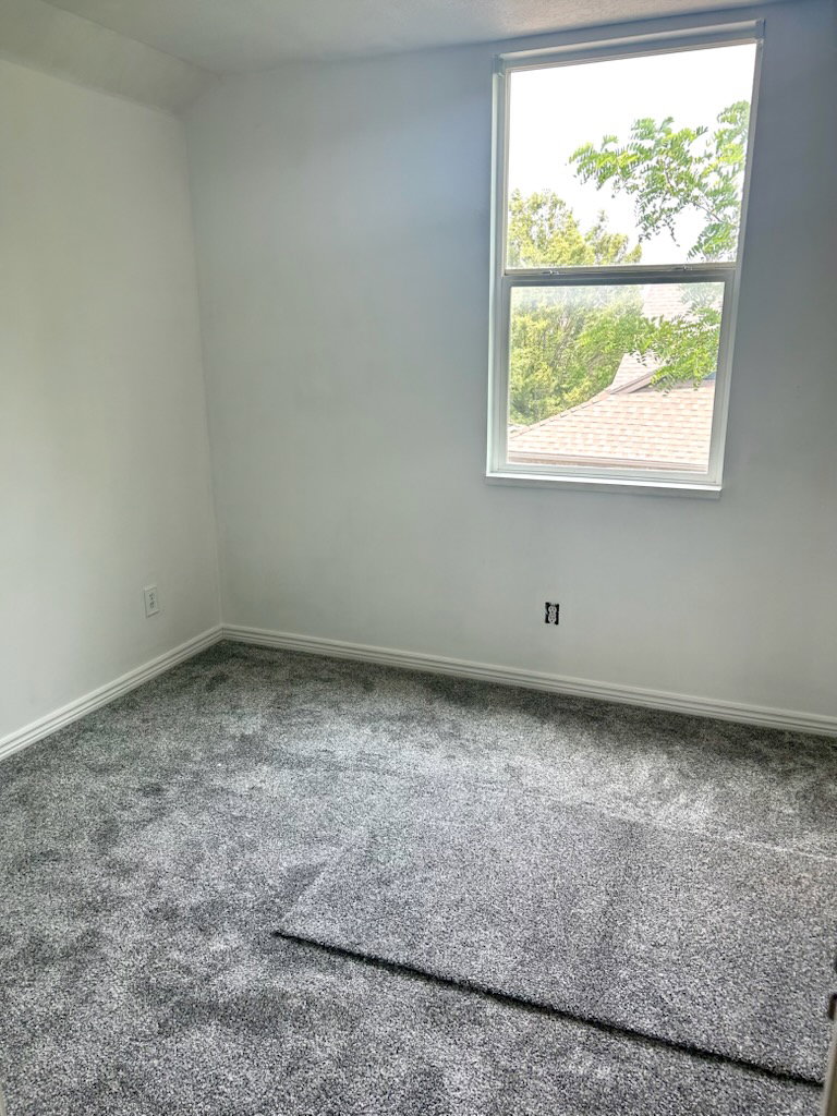 Bright room with new gray carpet, white walls, and a large window