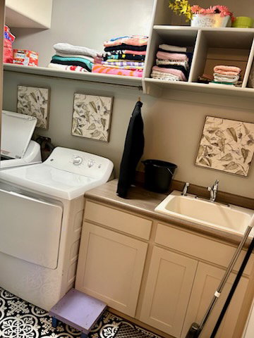 Dedicated laundry space featuring a utility sink, light-toned cabinetry, and dark countertop