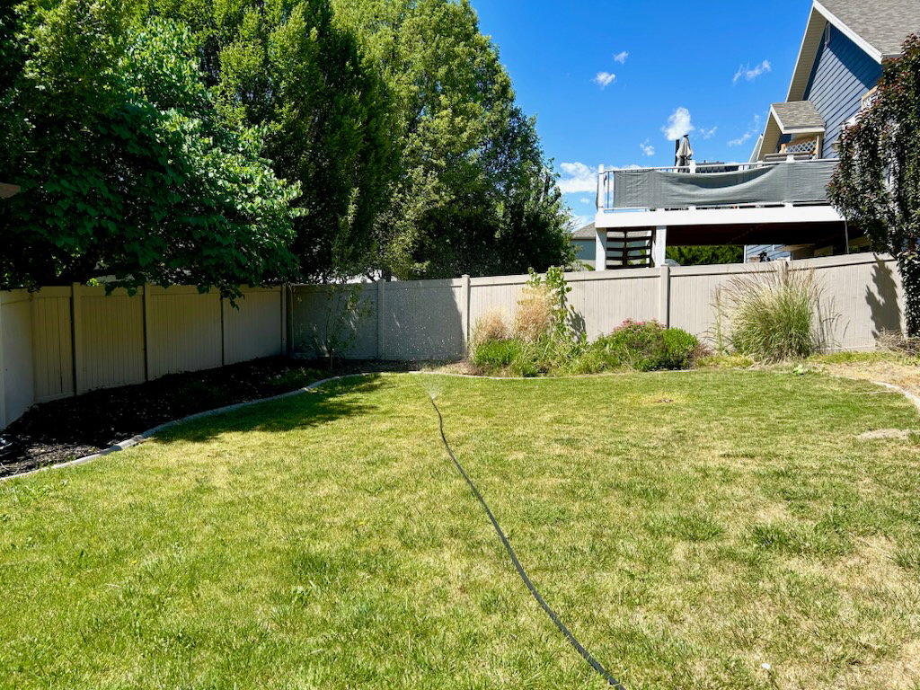 Spacious backyard featuring a manicured lawn, established perimeter landscaping, and a privacy fence