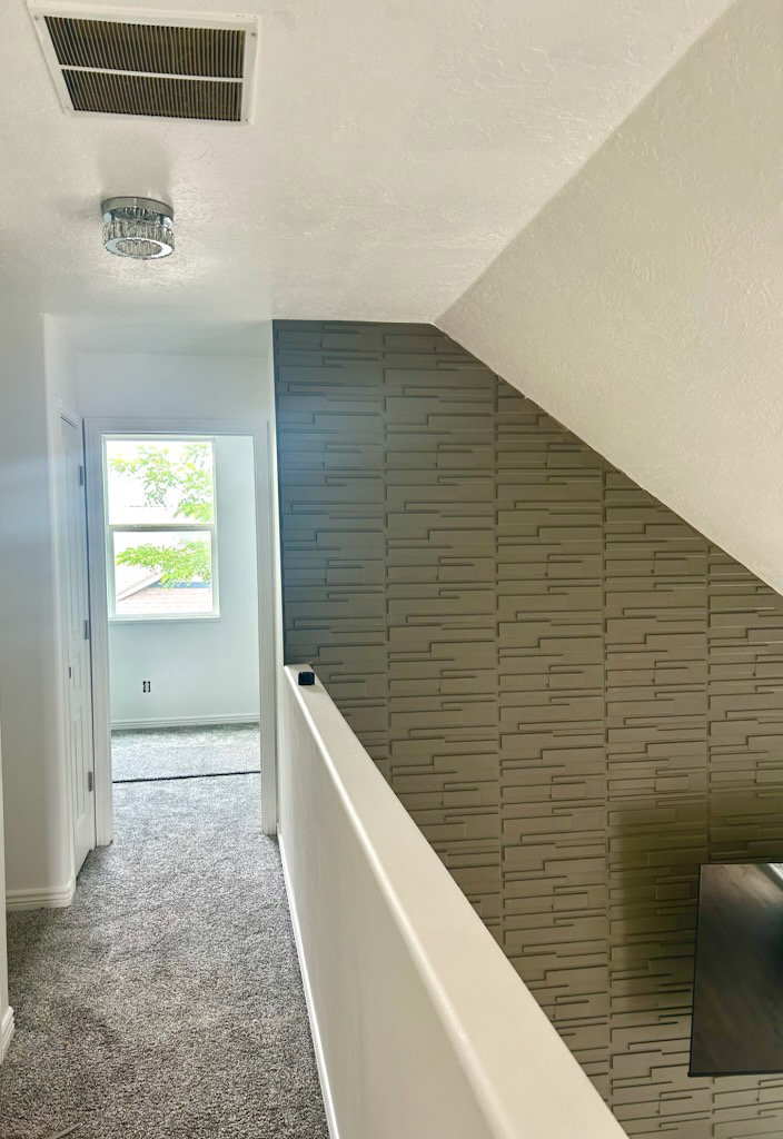 Upper-level hallway featuring textured wallpaper, white painted railings, and a window providing natural light