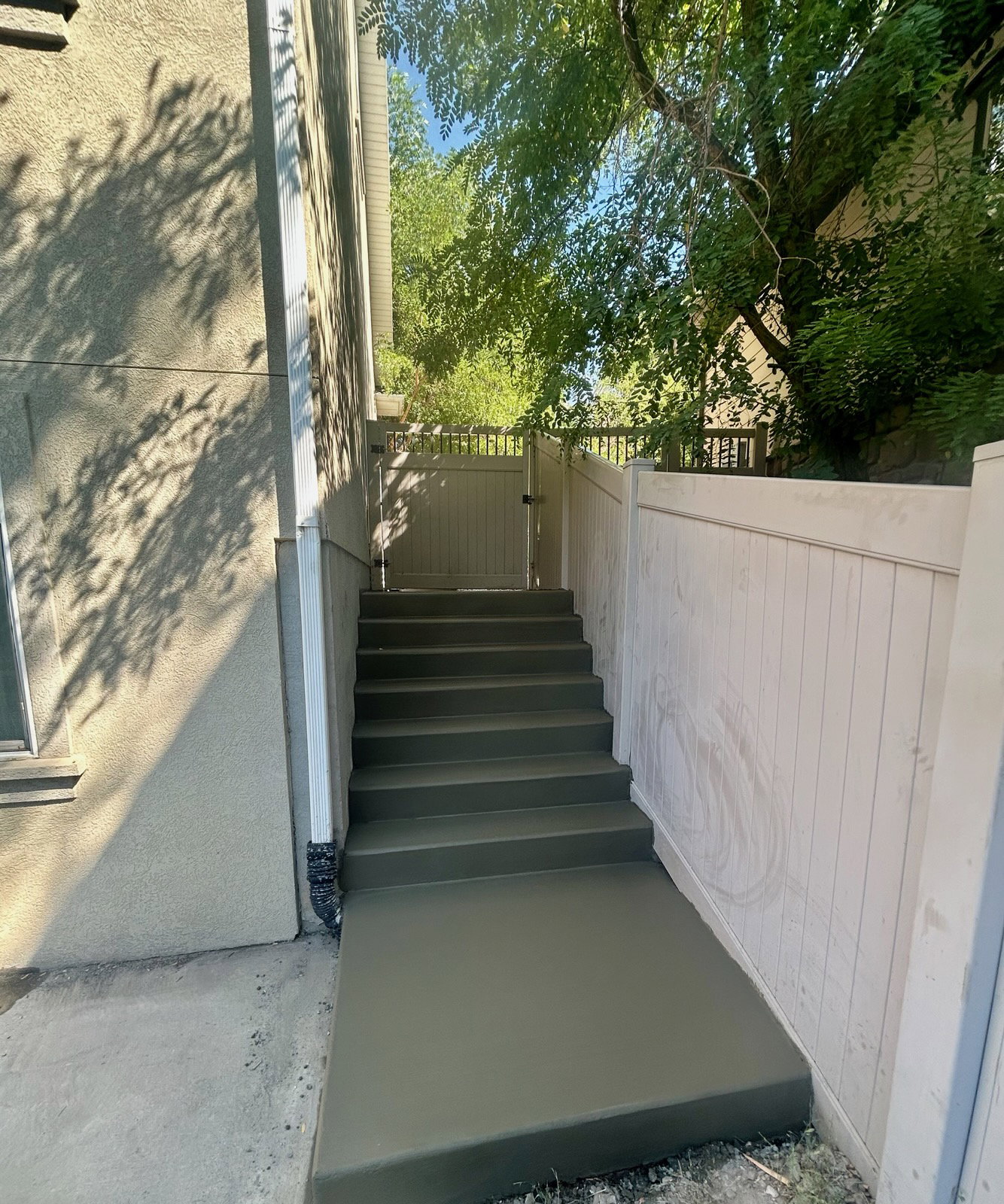 Exterior concrete stairs with a solid privacy fence and gate, bordered by stucco siding