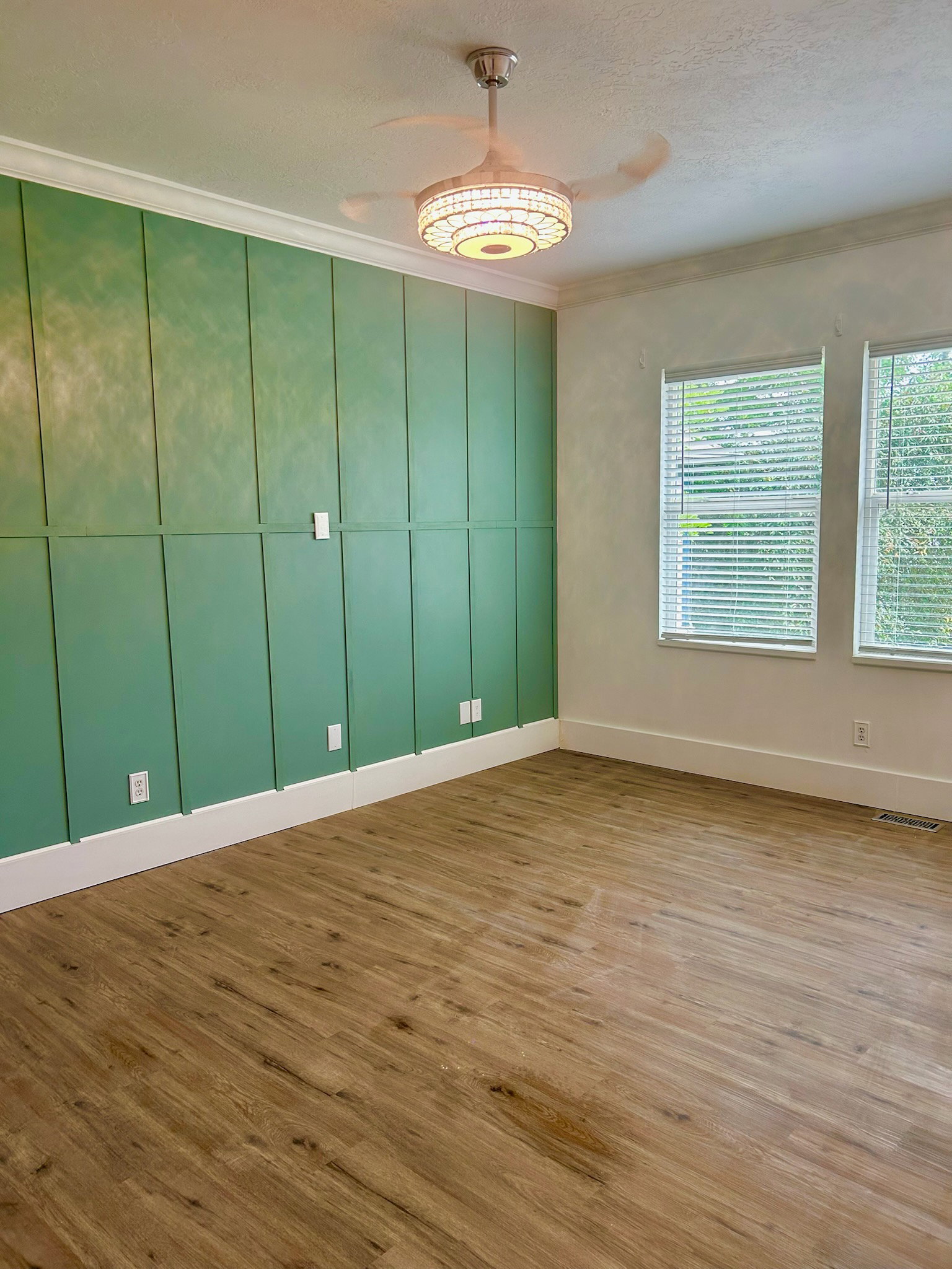 Spacious room featuring wood-finish flooring, a decorative paneled accent wall, and crown molding