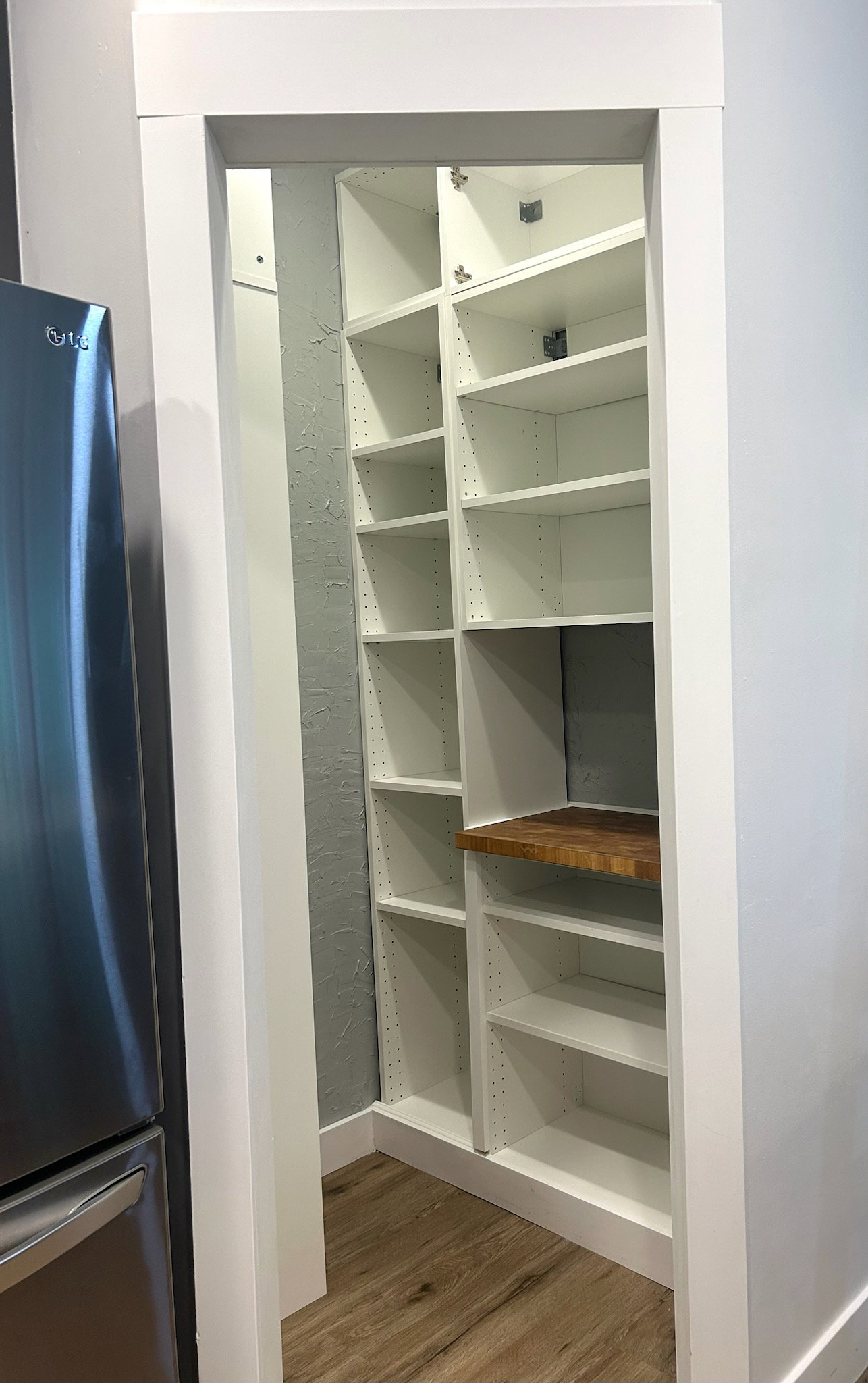 Walk-in pantry featuring white built-in shelving, a natural wood-finish countertop, and wood-finish flooring