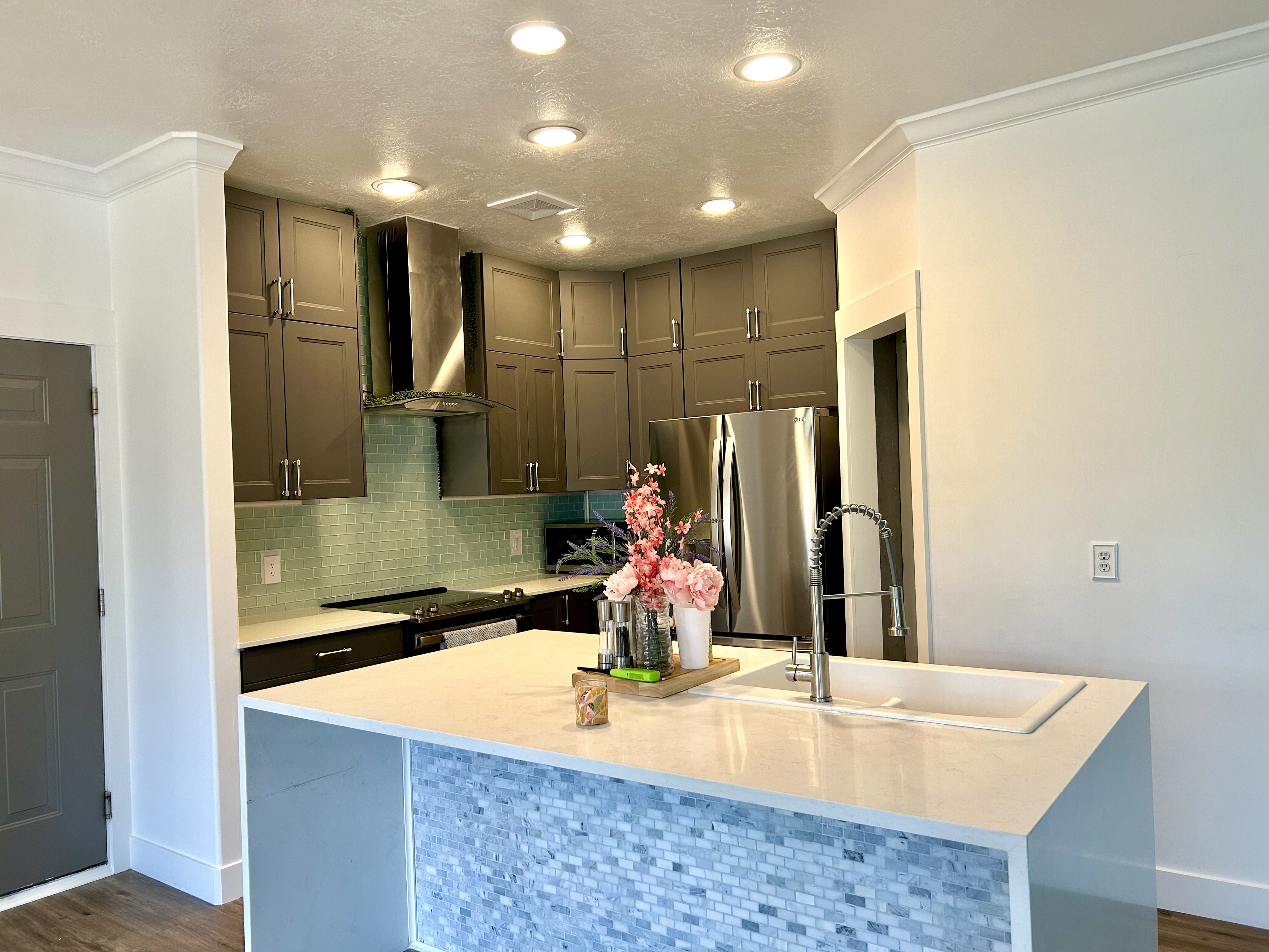 Modern kitchen featuring a white waterfall island with a mosaic tile accent, an integrated sink, and a gooseneck faucet