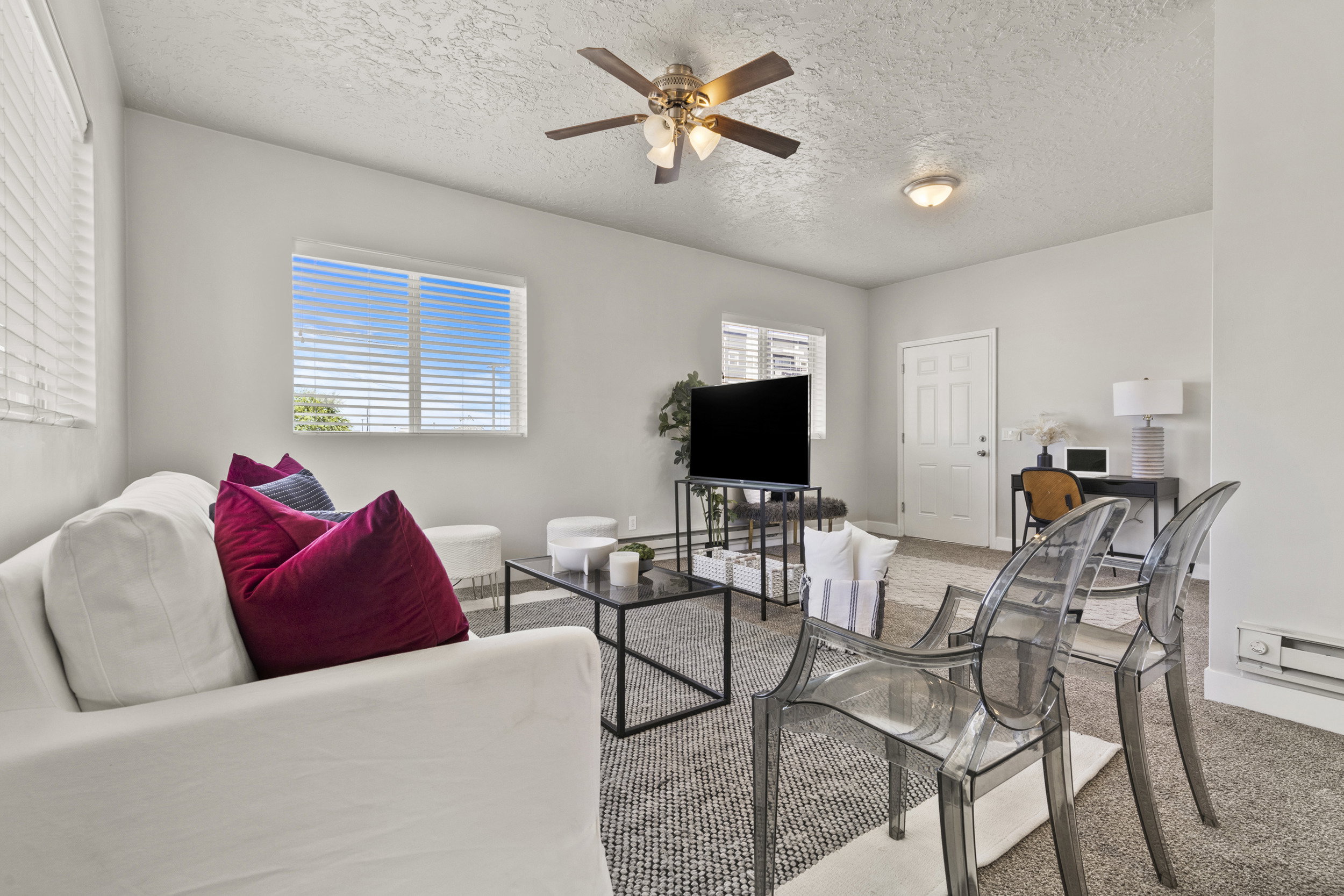 Living area featuring textured carpeting, light grey wall paint, and multiple windows with horizontal blinds
