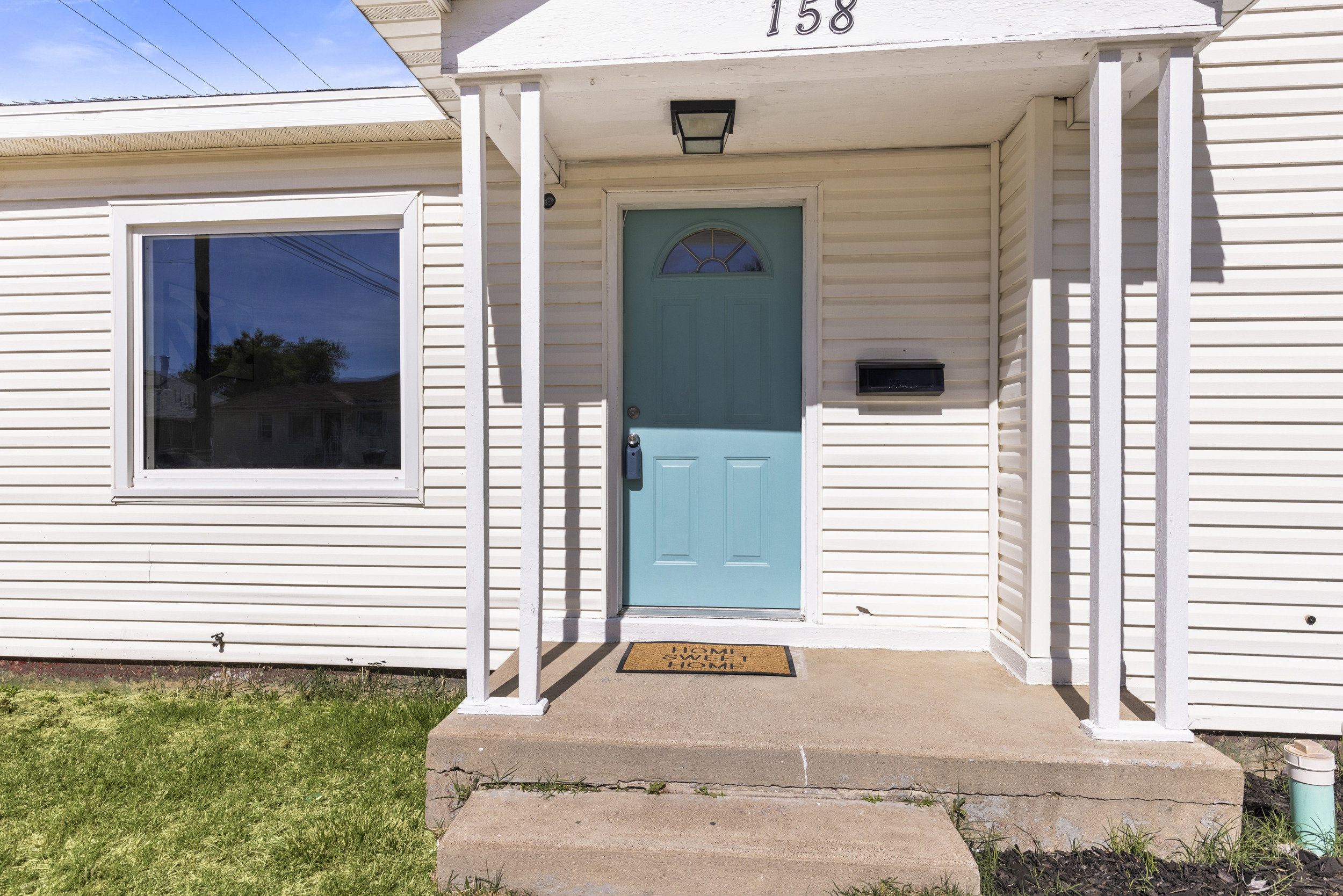 Front exterior featuring white horizontal siding, a vibrant blue entry door with an arched window, a covered porch with white columns, and a large single-pane window
