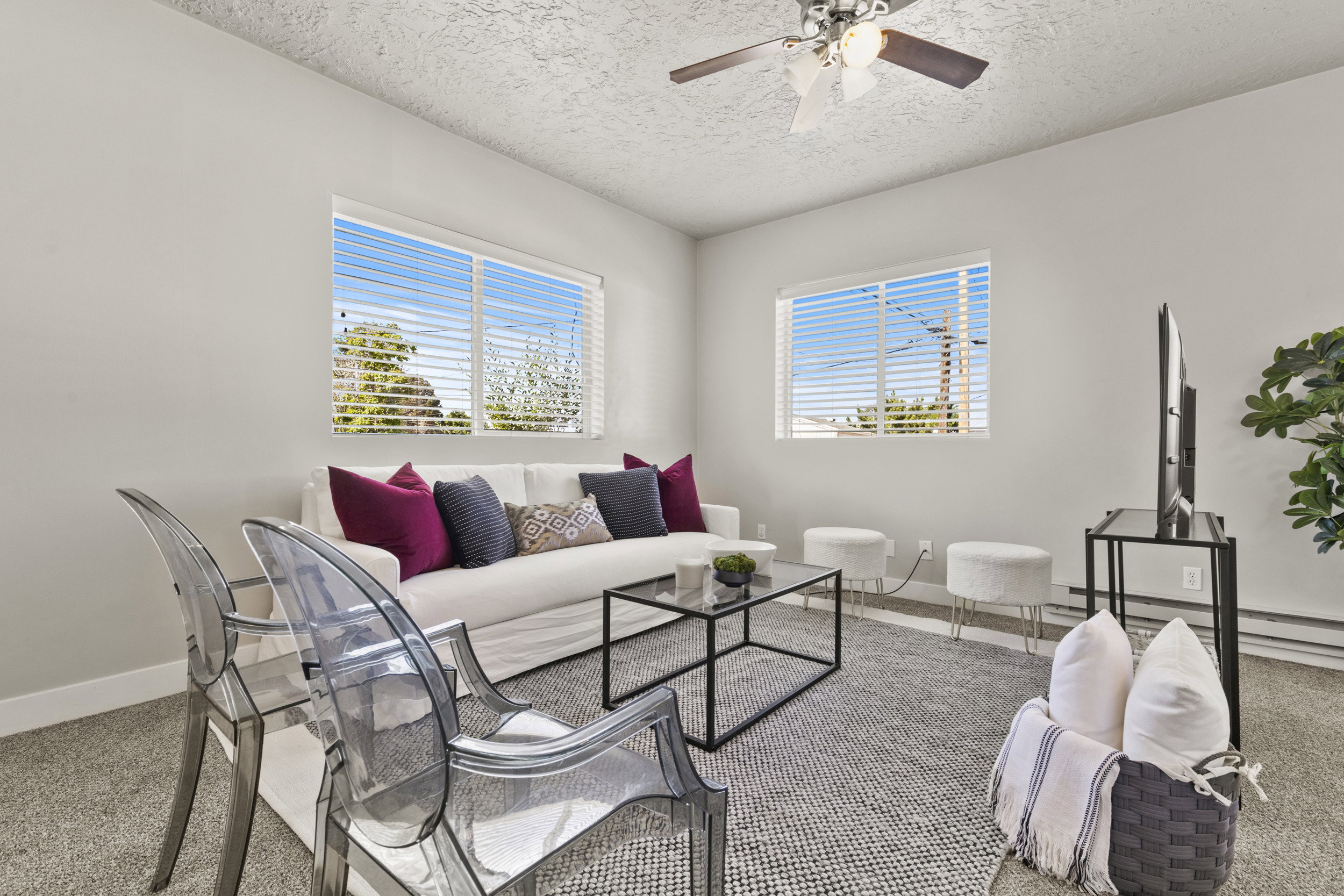 Living area featuring light gray walls, two bright windows with horizontal blinds, and a ceiling fan with light fixture
