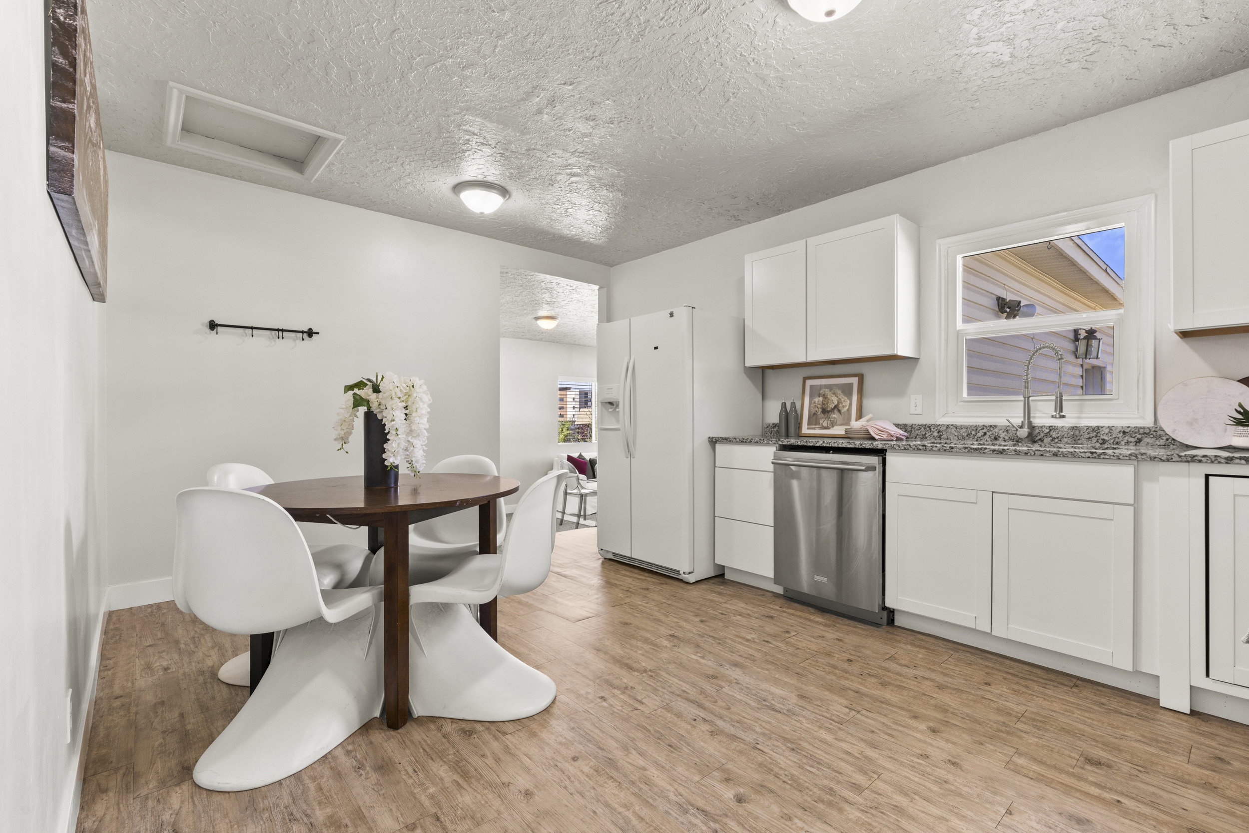 Kitchen and dining area featuring wood-finish flooring, white cabinetry, granite-patterned countertops, and a stainless steel dishwasher