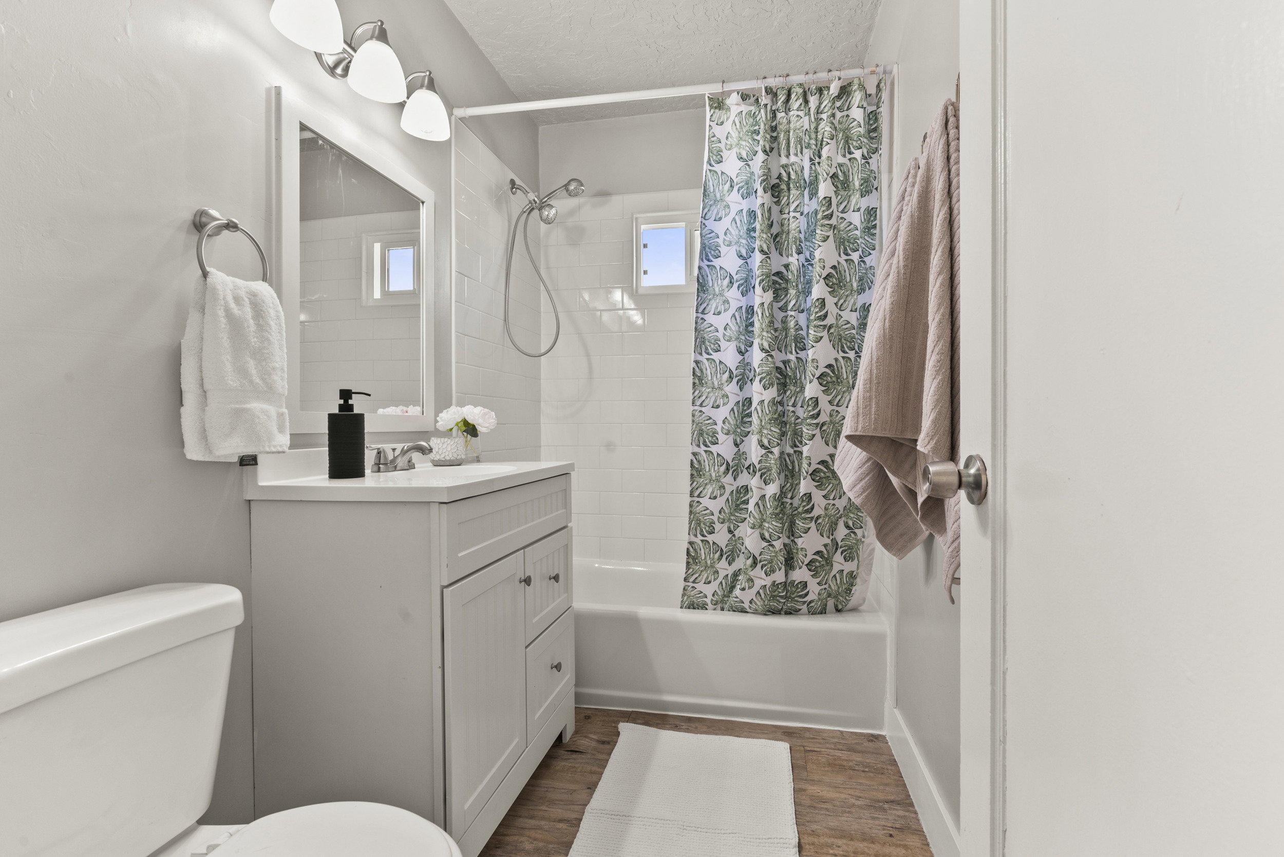 Bathroom featuring a white vanity with integrated sink, chrome faucet, wall-mounted mirror, and three-light fixture