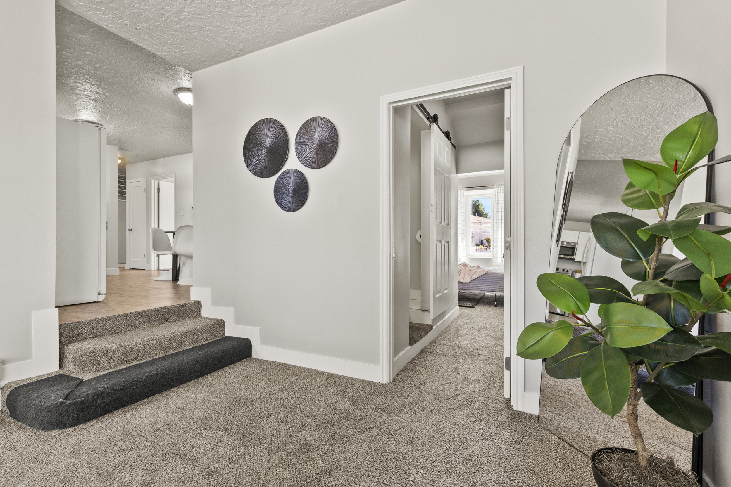 Carpeted hallway with a staircase featuring a carpeted runner, white walls, and a sliding barn door entryway