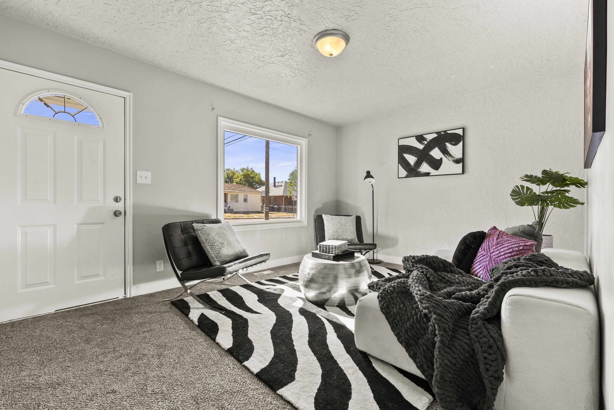Living area featuring neutral wall paint, carpet flooring, a white paneled door with an arched glass insert, and a large window