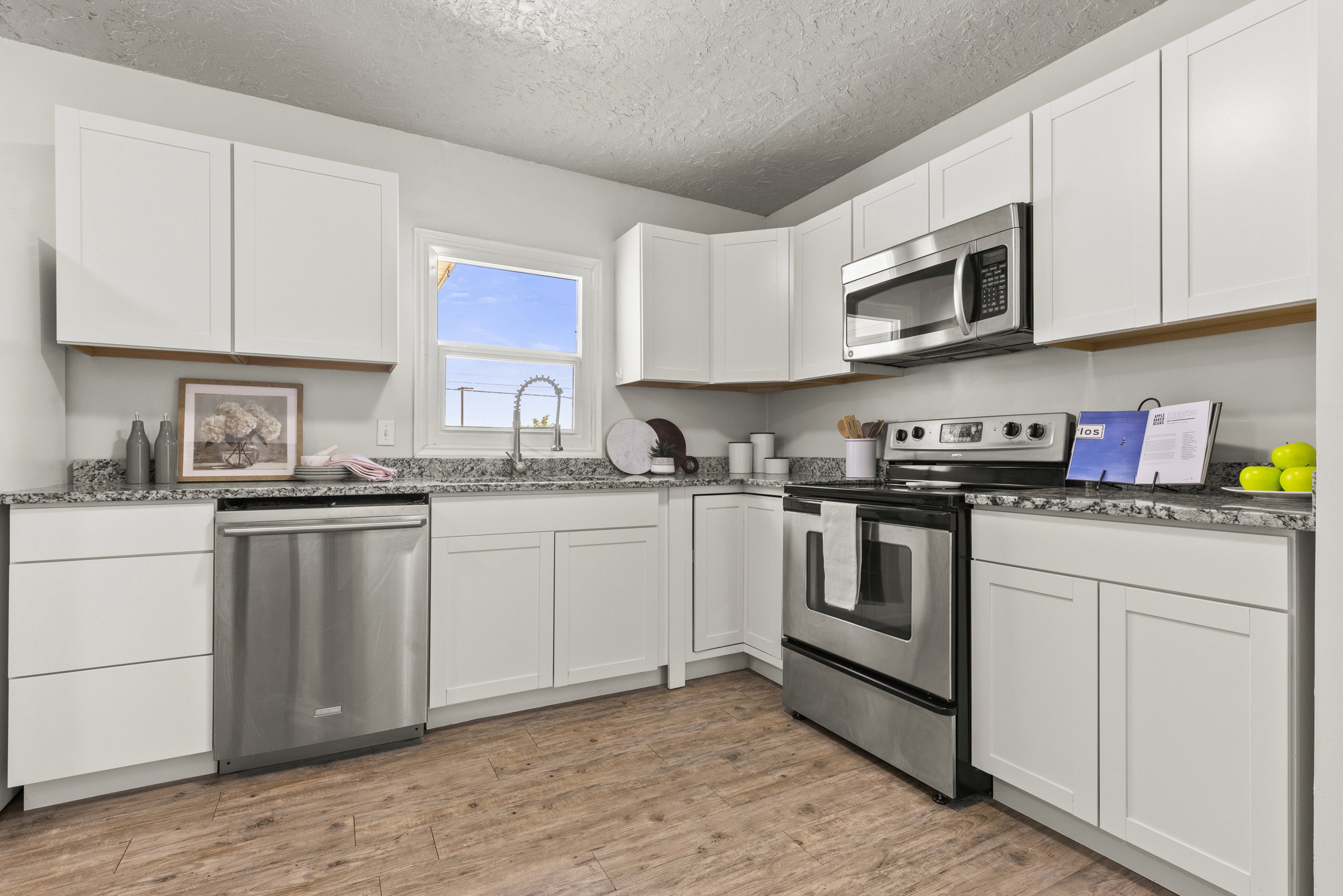 Kitchen featuring white cabinetry, grey speckled countertops, stainless steel appliances, and wood-finish flooring