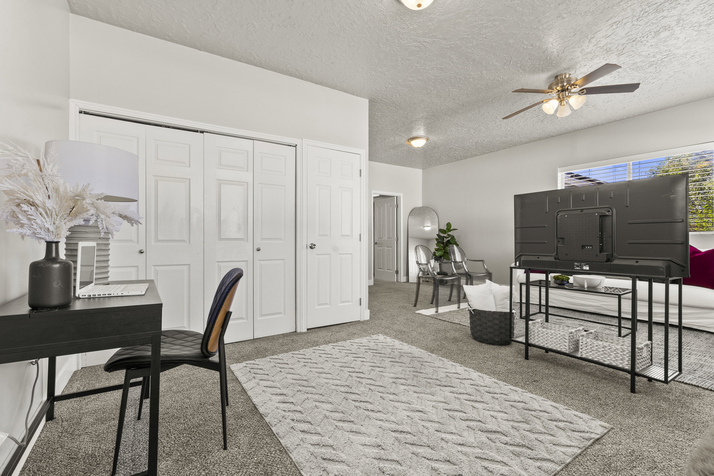 Spacious room featuring carpeted flooring, multiple bi-fold closet doors, a ceiling fan with integrated lighting, and natural light from a window