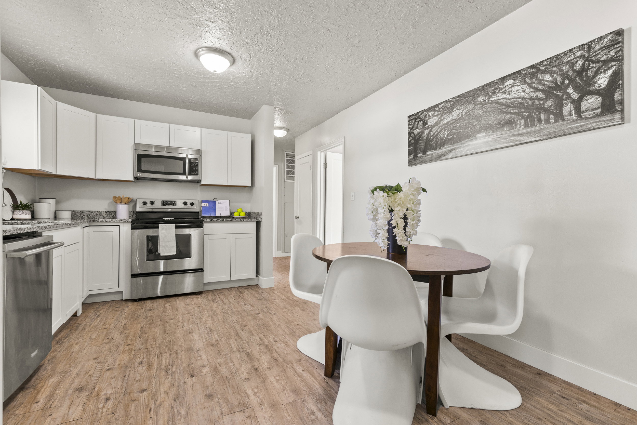 Kitchen and dining area featuring wood-finish flooring, white cabinetry, stainless steel appliances, and light-toned countertops