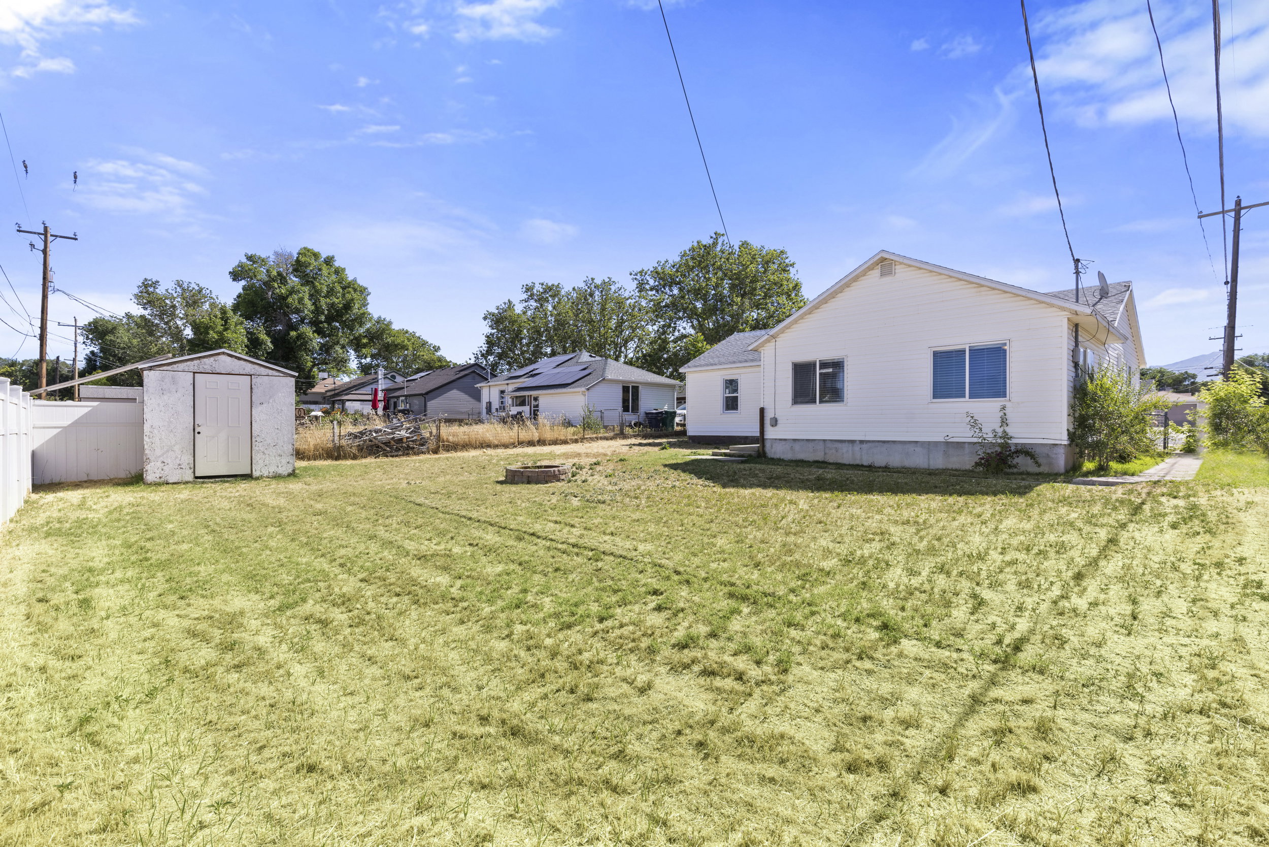 Expansive backyard featuring a white privacy fence, a detached storage shed, and a fire pit