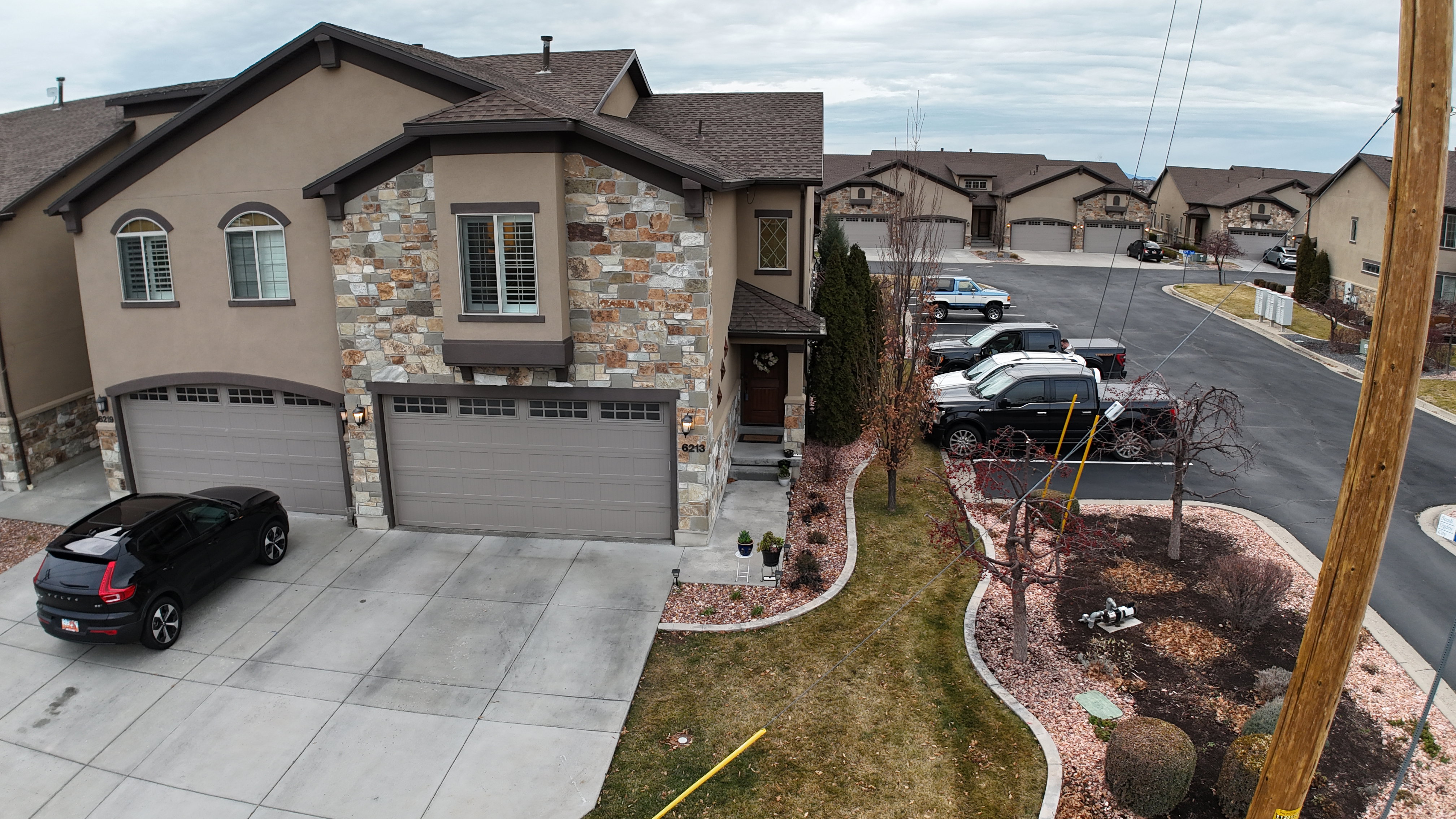 Stucco and stone facade with multiple garage doors, a covered entry, and landscaped front yard
