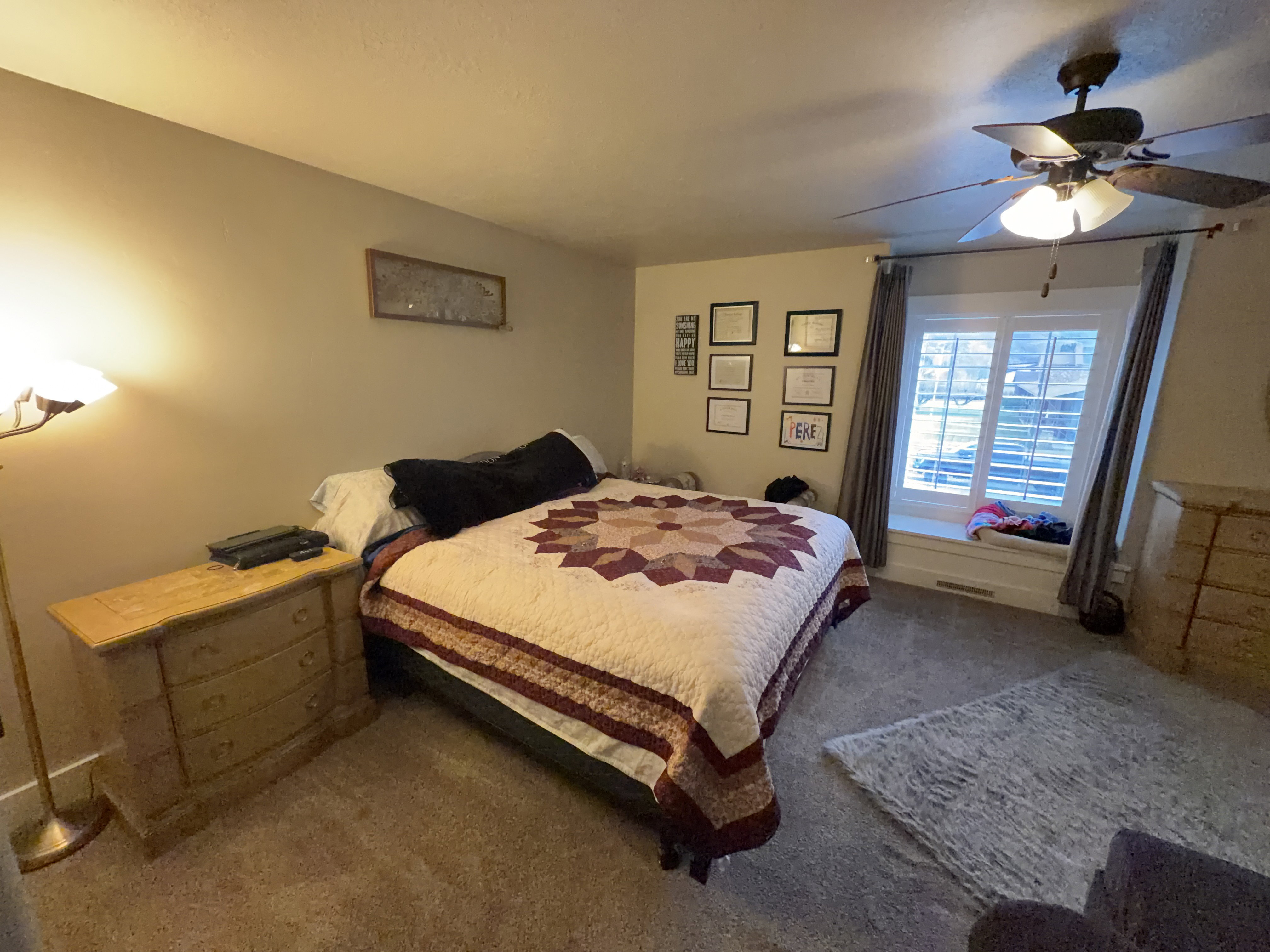 Carpeted room featuring a window with a built-in window seat, ceiling fan with light fixture, and neutral wall tones
