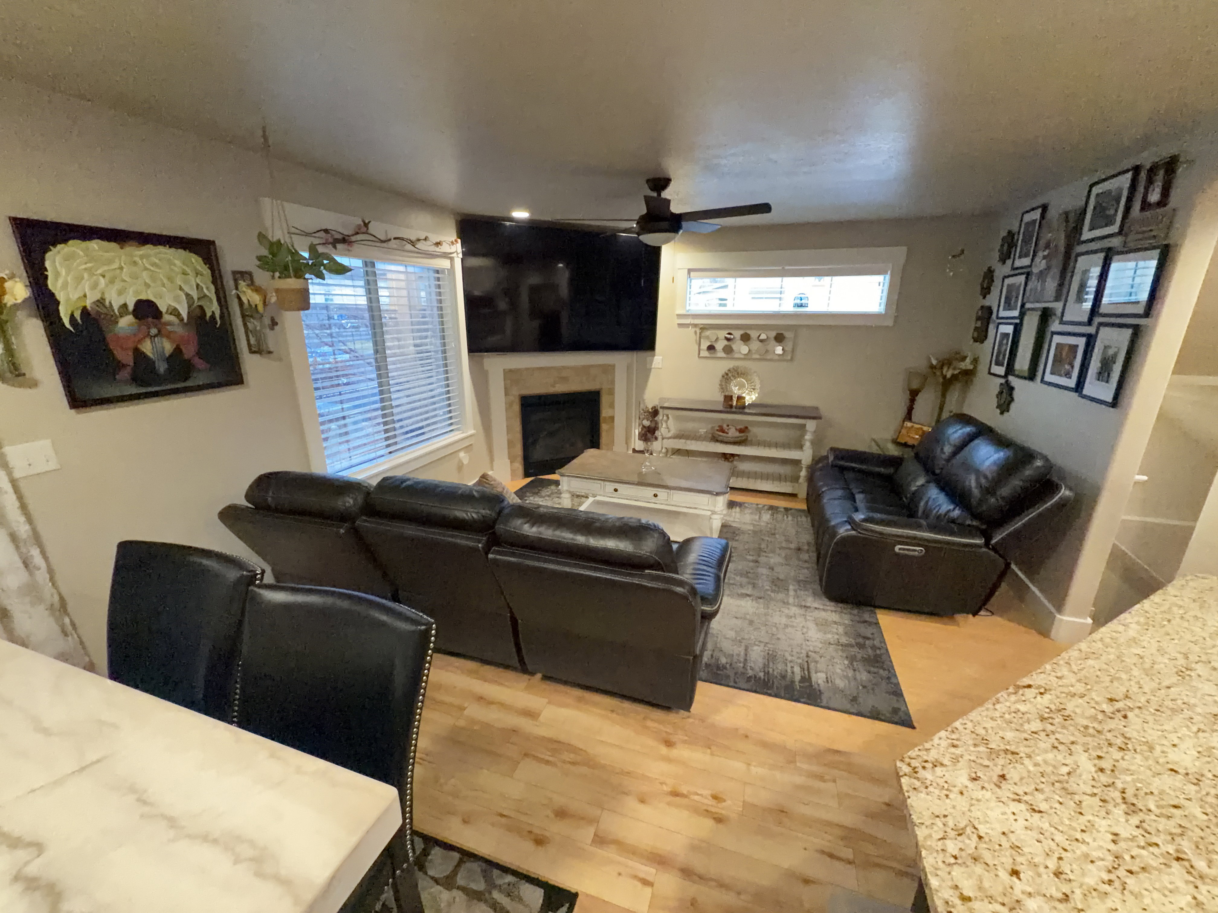 Living area with wood-finish flooring, a ceiling fan with integrated lighting, and a fireplace featuring a stone surround and mantel