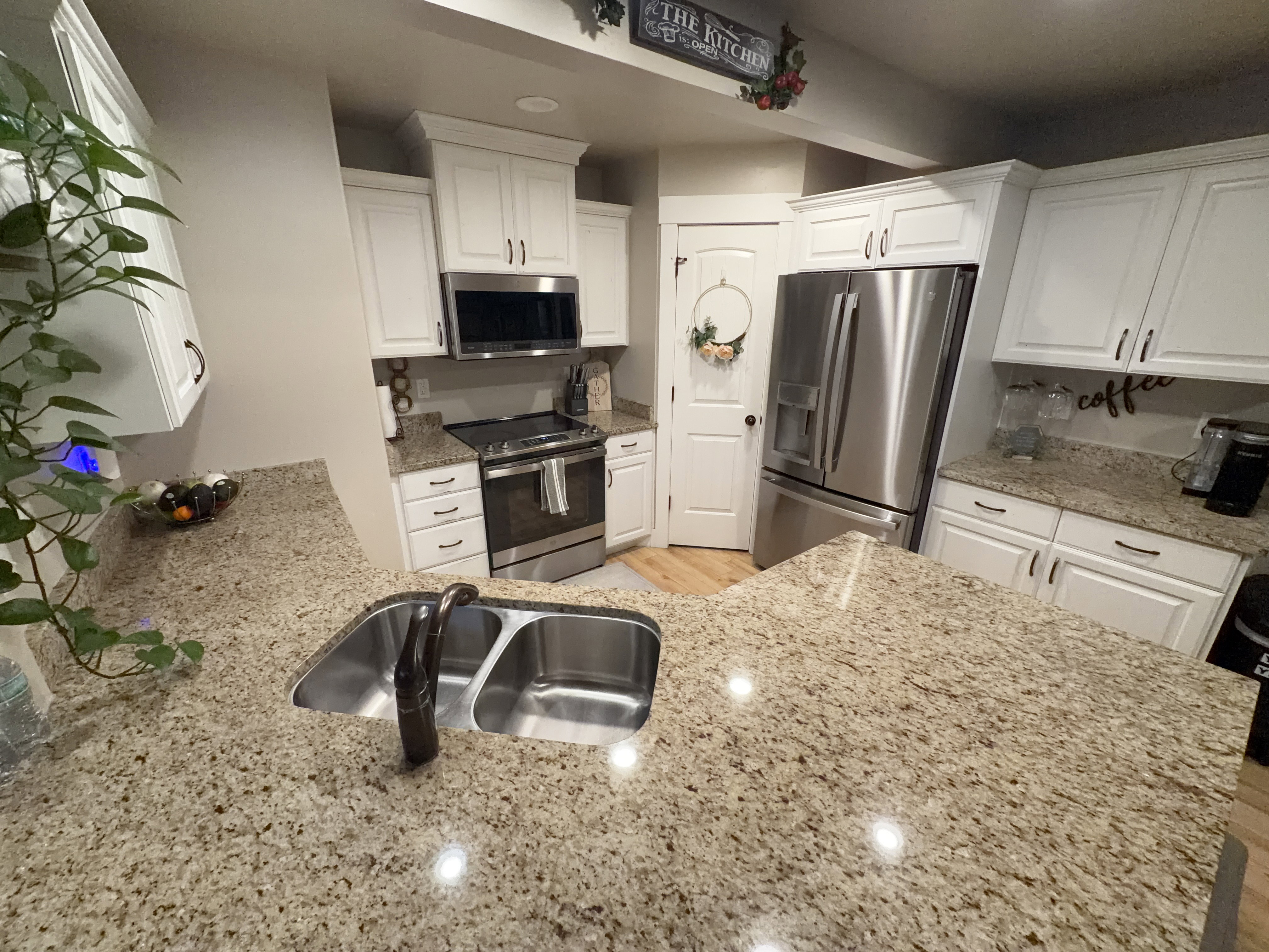 Kitchen featuring light-toned granite countertops, white cabinetry, a double basin stainless steel sink, and stainless steel appliances