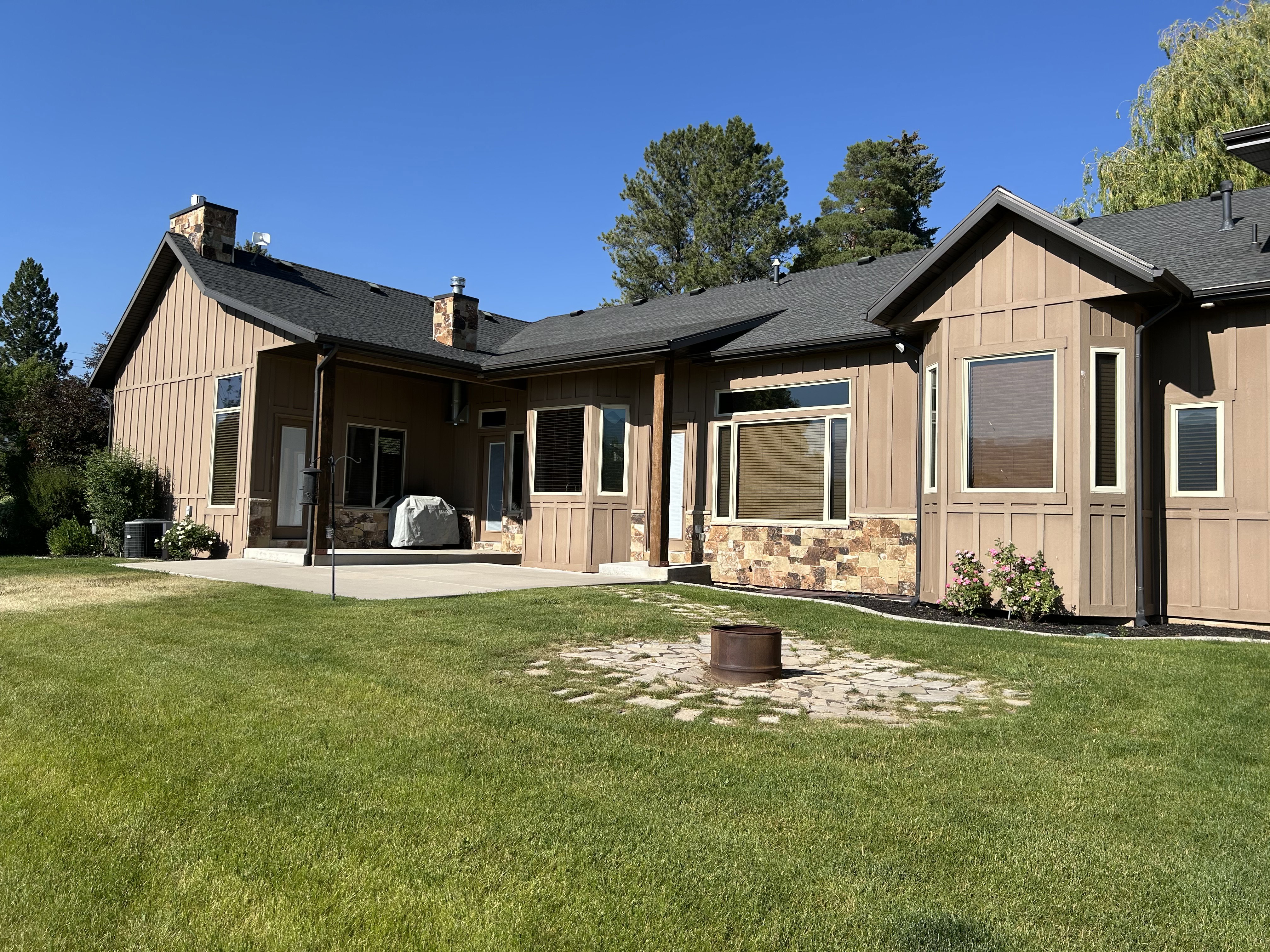 Expansive rear exterior featuring a concrete patio, board and batten siding, stone veneer accents, and multiple windows