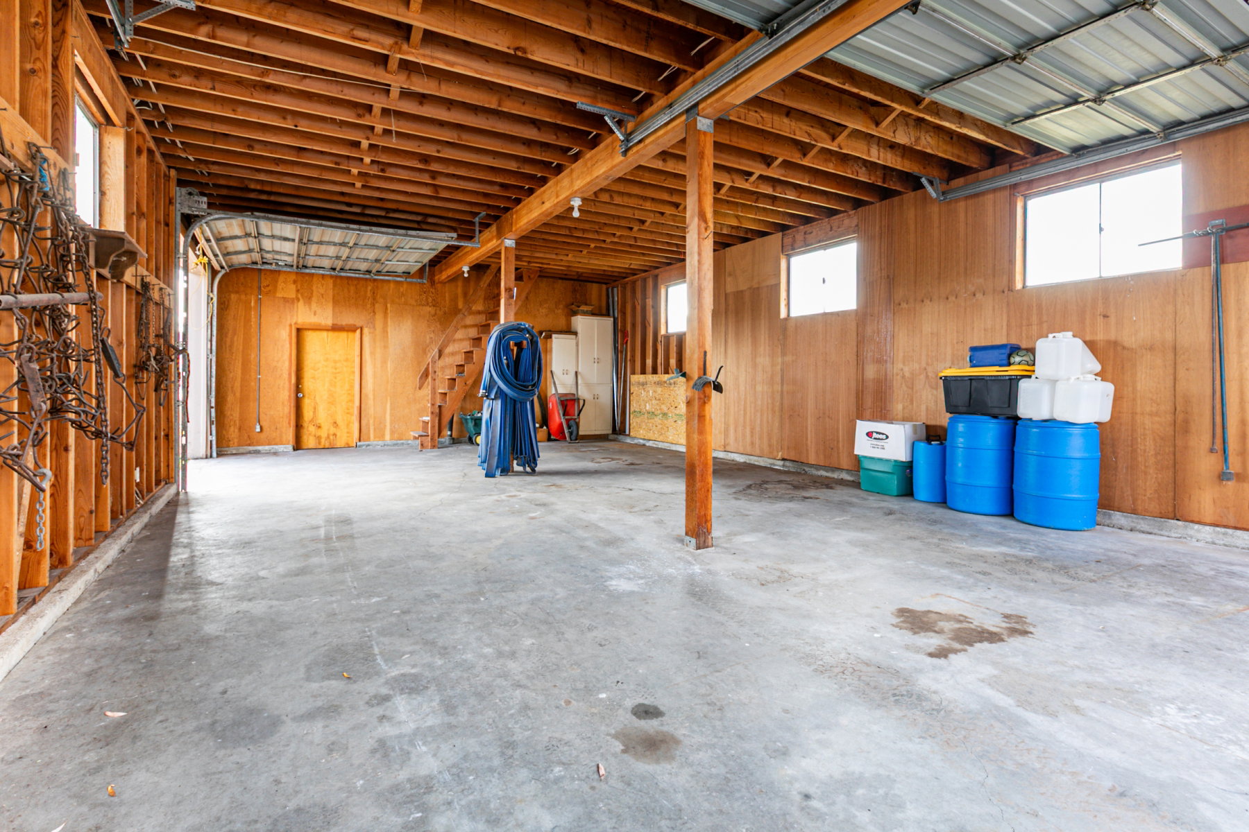 Spacious open garage with concrete flooring, exposed wood beam ceiling, and wood paneling
