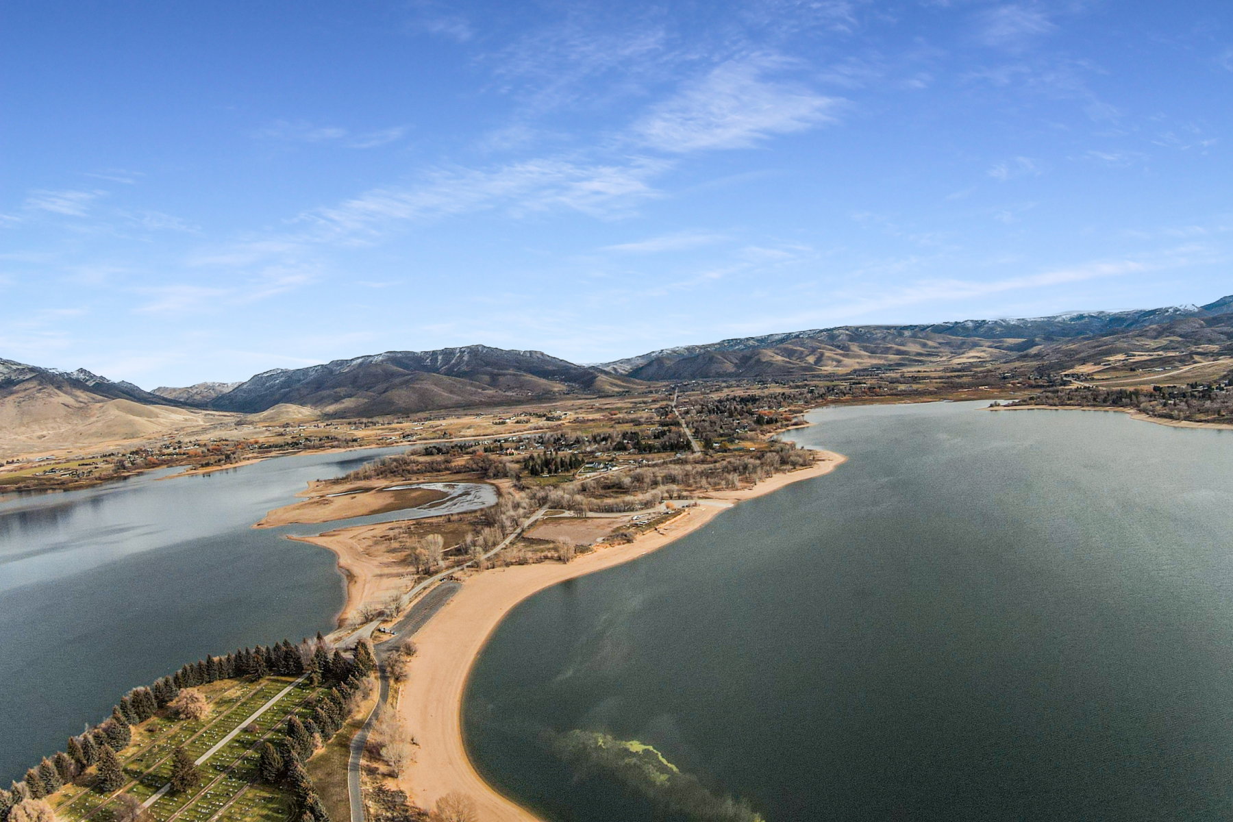 Expansive lake with surrounding land featuring sandy shores, wooded areas, and distant mountains