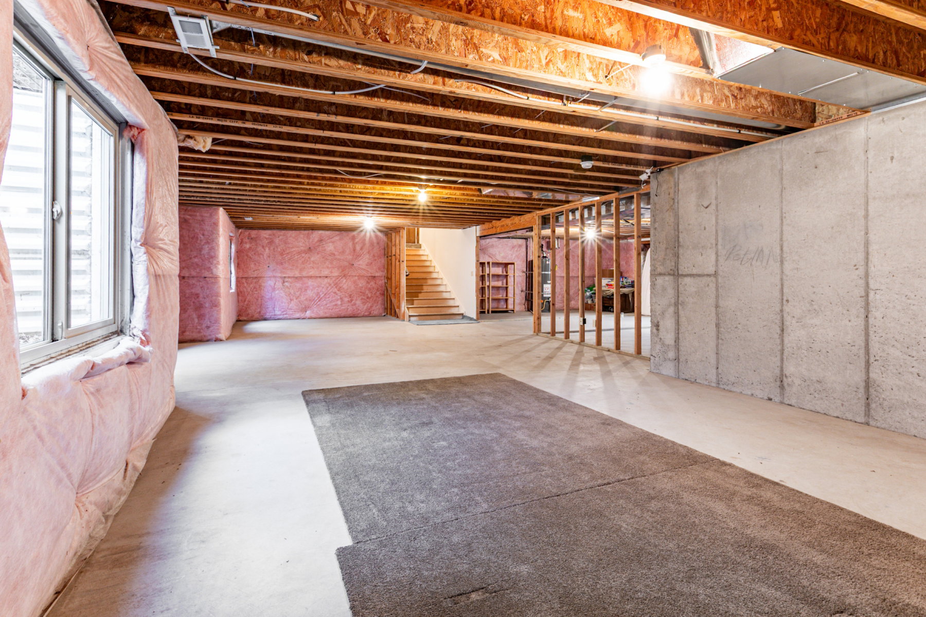 Lower level area featuring exposed wood joists, concrete flooring, and insulated walls