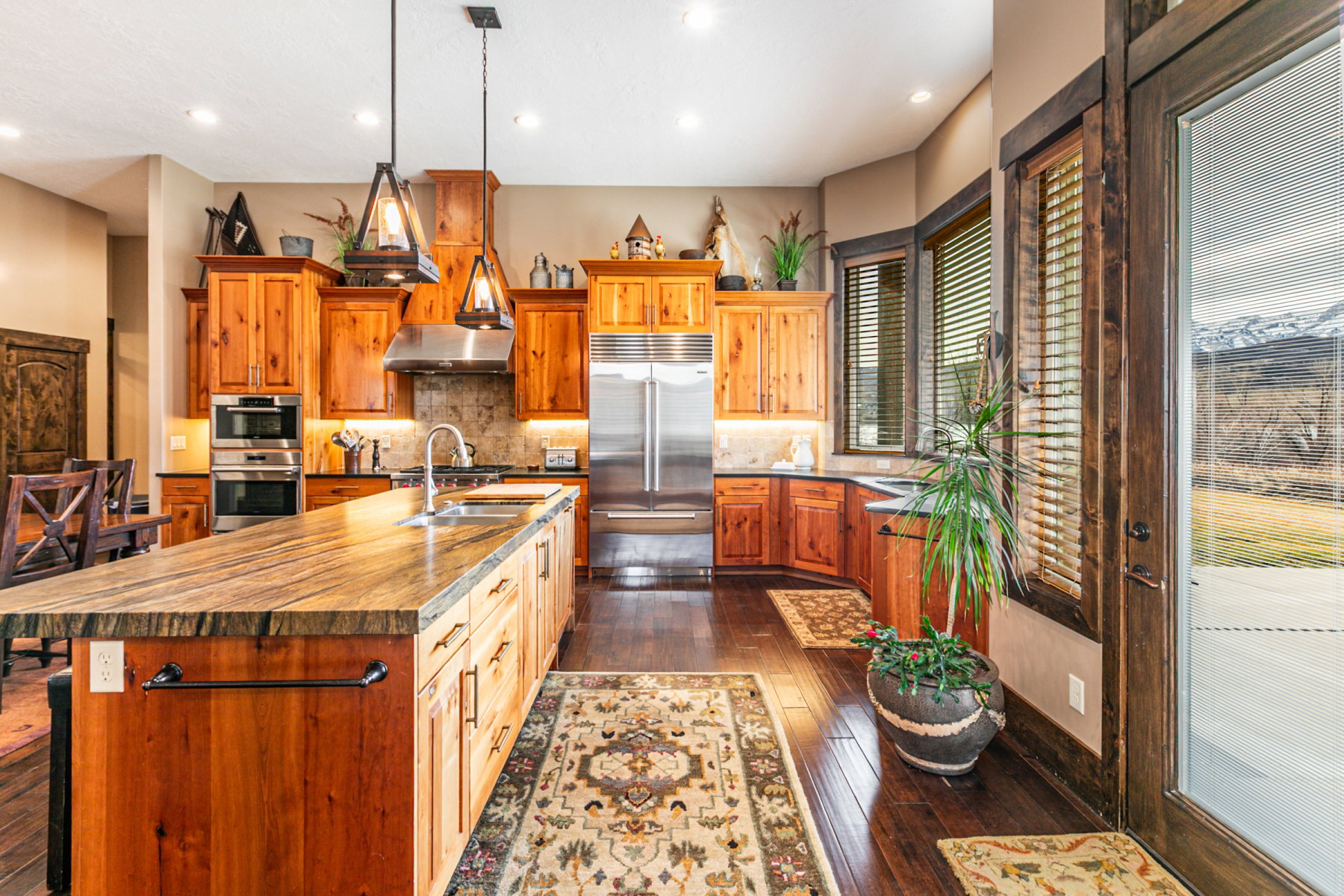 Gourmet kitchen featuring a large central island with a built-in sink, stainless steel appliances, rich wood cabinetry, dark wood-finish flooring, and recessed lighting