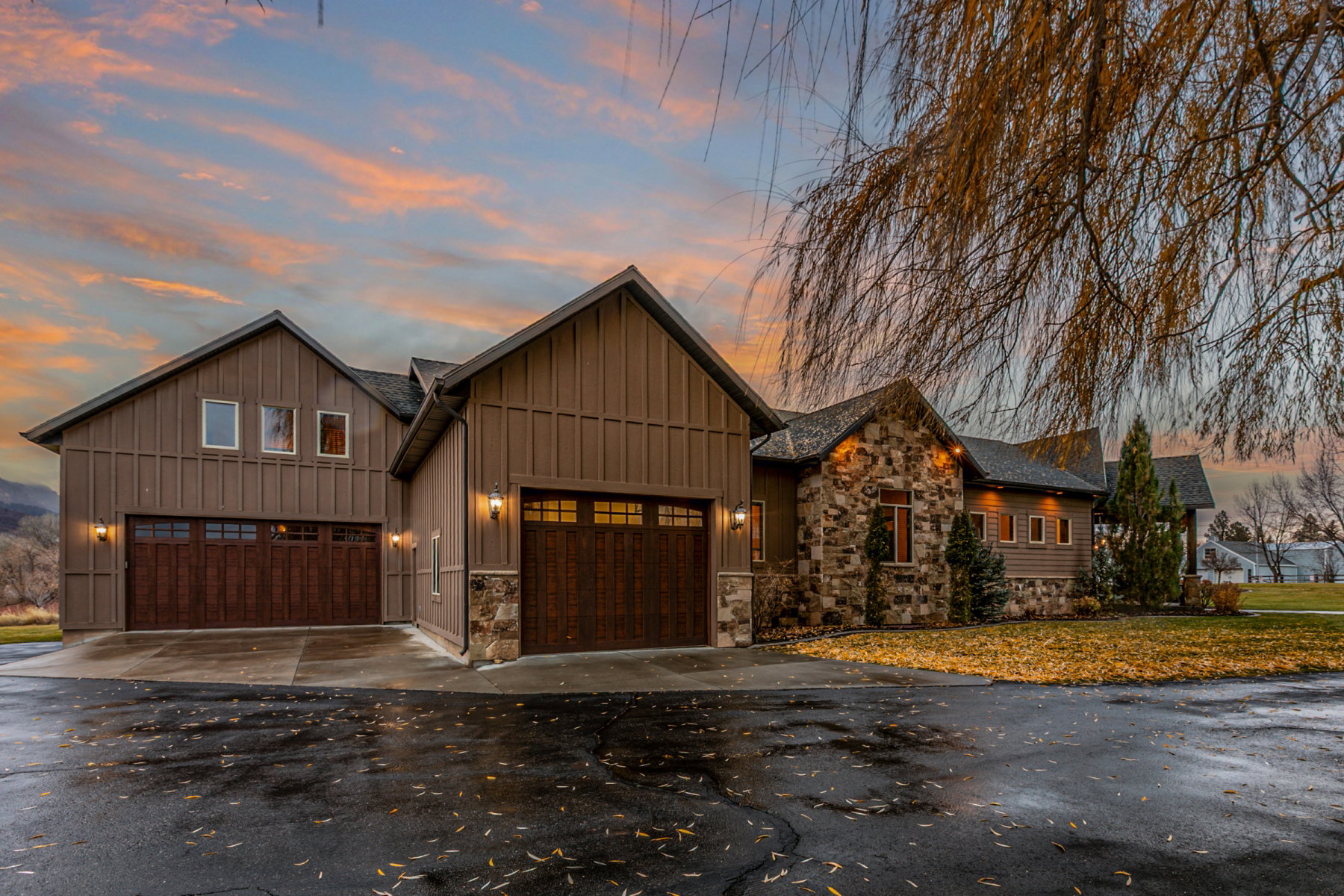 Exterior featuring board and batten siding, stone accents, two attached garages with wood-finish doors, and multiple windows