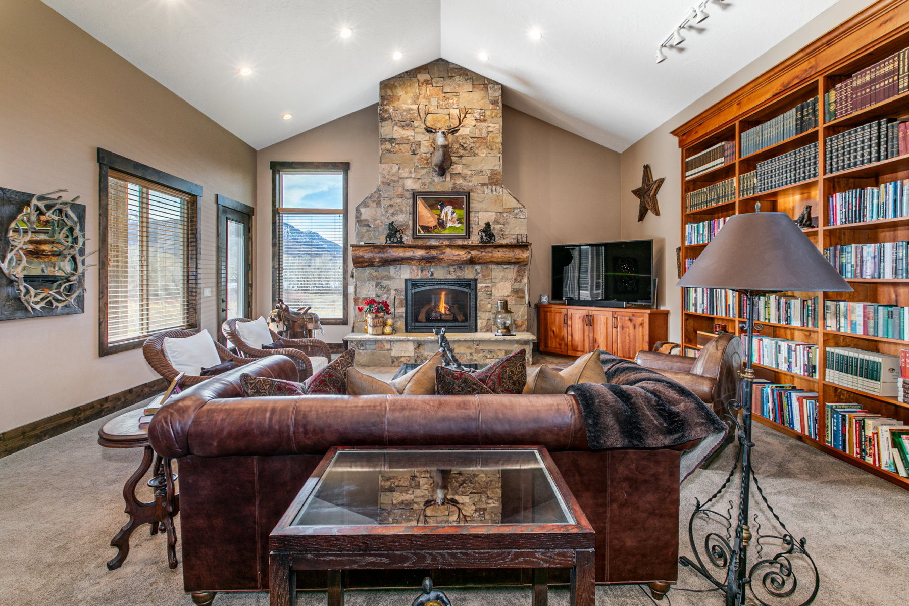 Vaulted ceiling great room featuring a stone fireplace, built-in timber mantel, and an extensive custom wood bookcase
