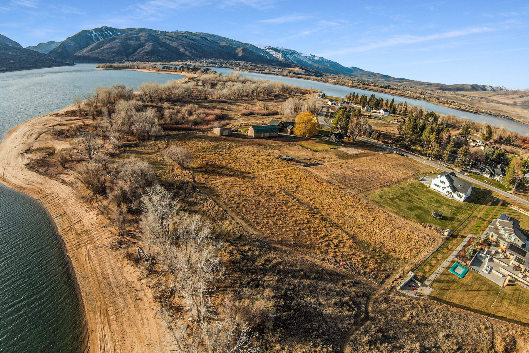Expansive waterfront property featuring a substantial land parcel, direct water access, mature trees, a visible structure with a green roof, and distant mountain backdrops