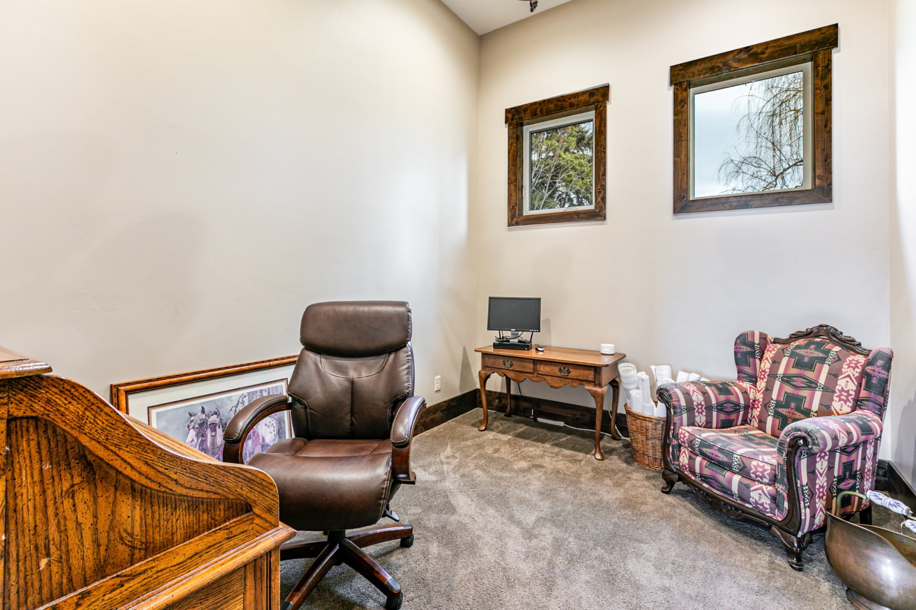 Recessed lighting illuminates a neutral-toned room featuring two framed windows with natural wood trim