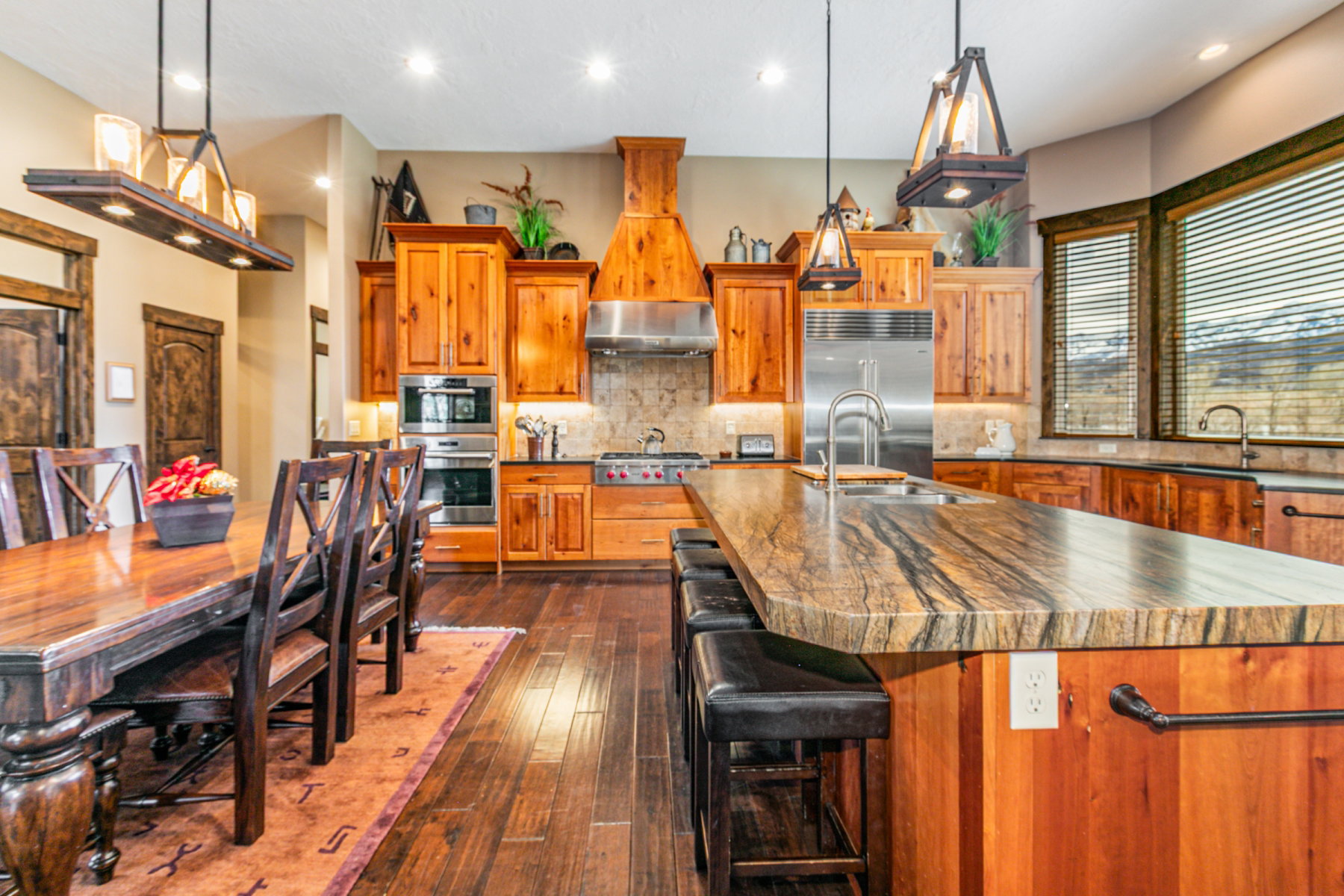 Gourmet kitchen and dining area featuring rich wood-finish flooring, custom wood cabinetry, and a substantial island with stone countertop