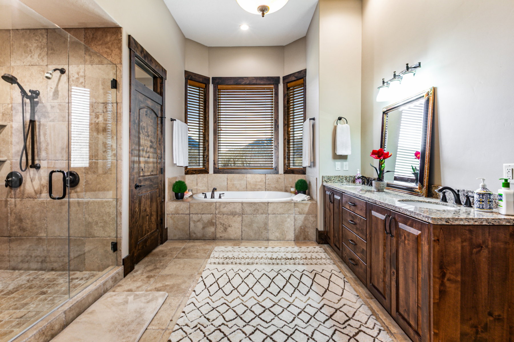 Spacious bathroom featuring a built-in soaking tub, separate glass-enclosed shower, dual vanity with undermount sinks and stone countertop, and large format tile flooring