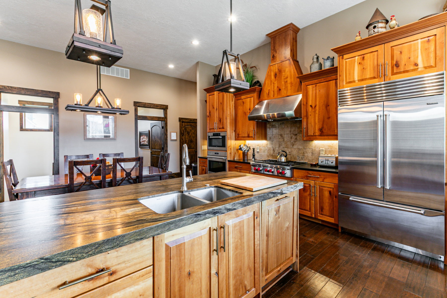 Gourmet kitchen featuring a large central island with double sink, custom wood cabinetry, stainless steel appliances, and wood-finish flooring