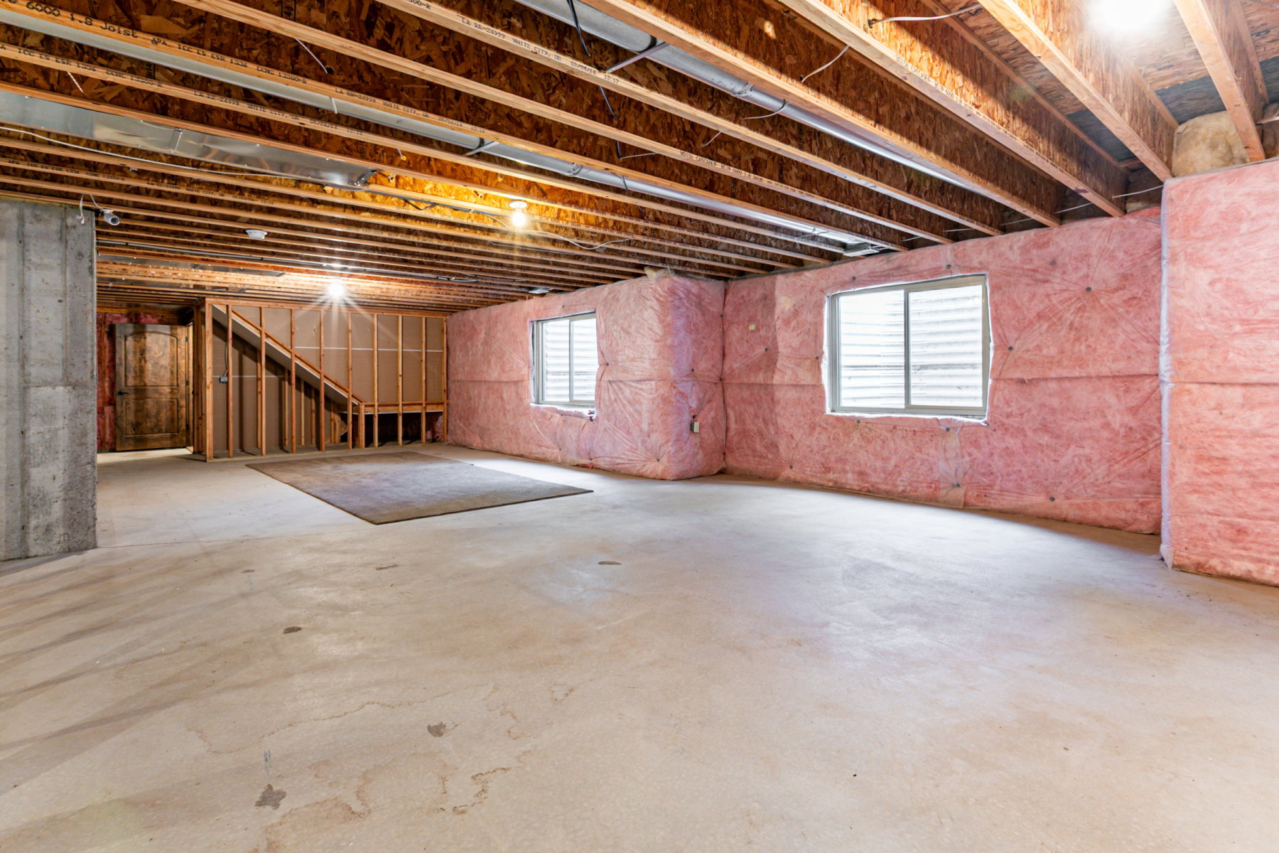 Unfinished basement with concrete flooring, exposed wooden ceiling joists, and insulated perimeter walls