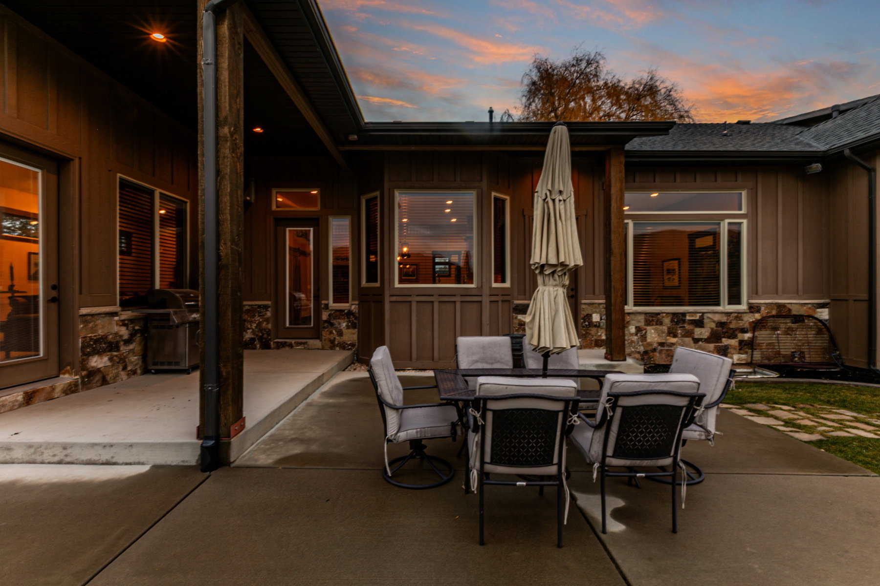 Expansive concrete patio with covered and uncovered areas, board and batten siding, stone veneer accents, and recessed lighting