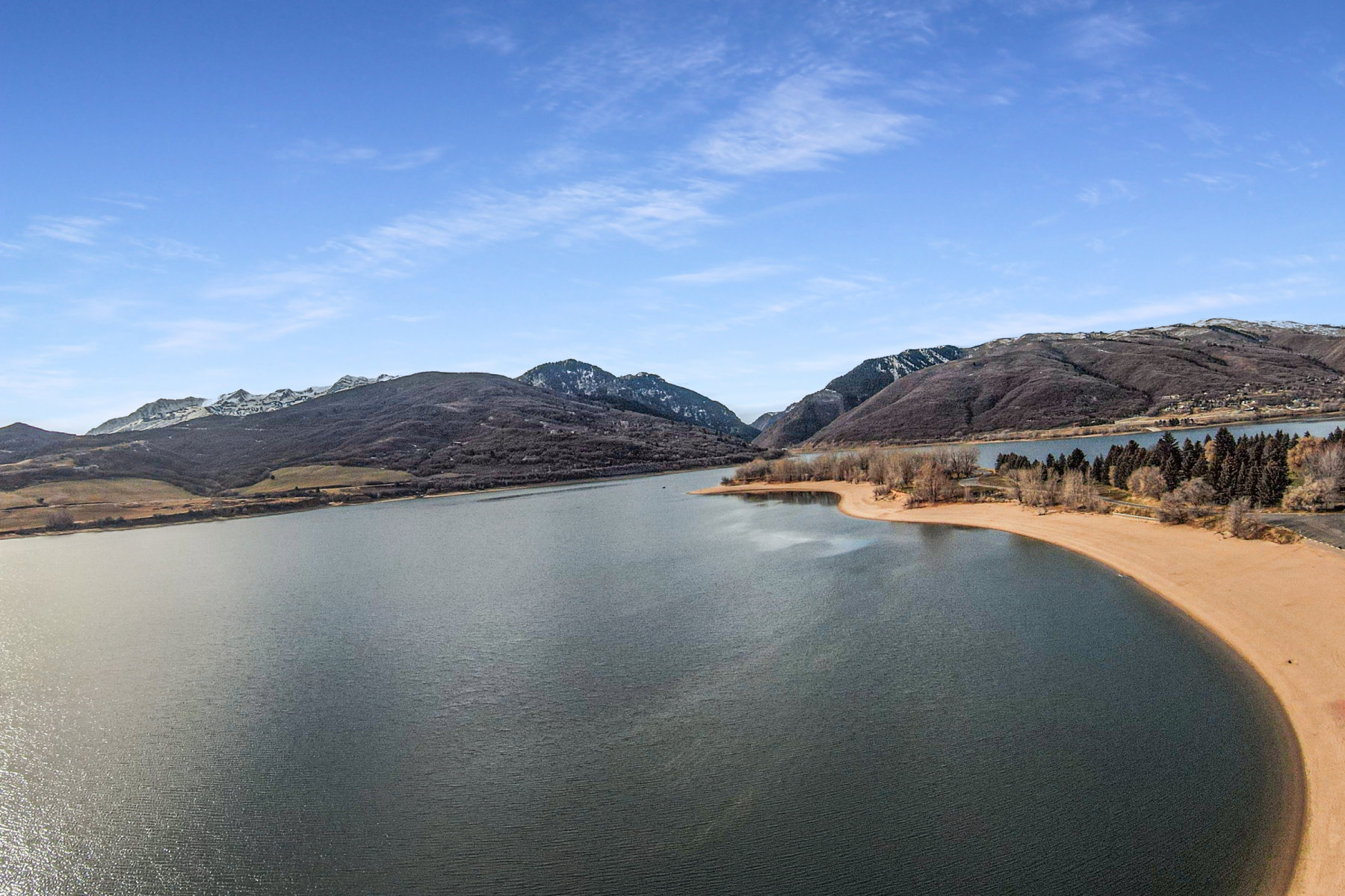Expansive waterfront property featuring a sandy shoreline and surrounding mountain ranges