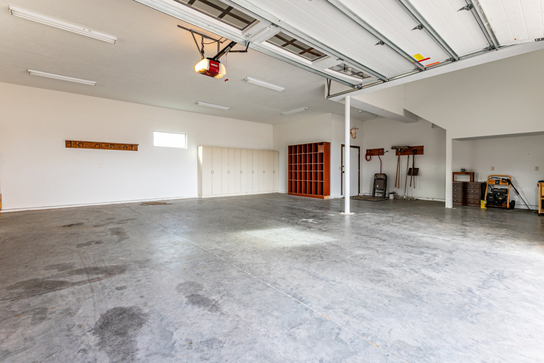 Spacious garage with exposed concrete flooring, overhead fluorescent lighting, and a white paneled garage door opener