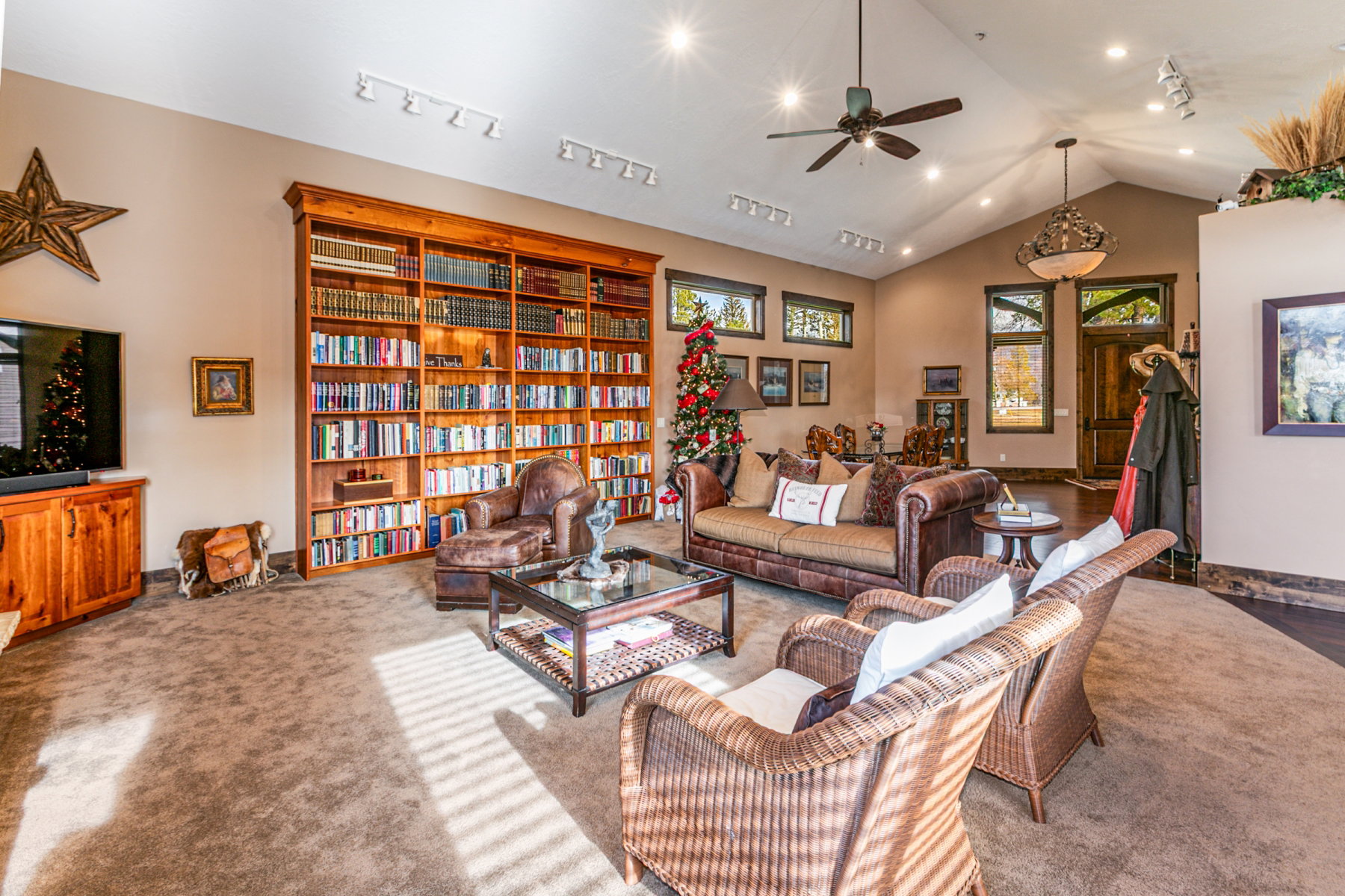 Spacious living area featuring a full-height built-in wood bookcase, vaulted ceilings, recessed lighting, a ceiling fan, and wood-trim windows