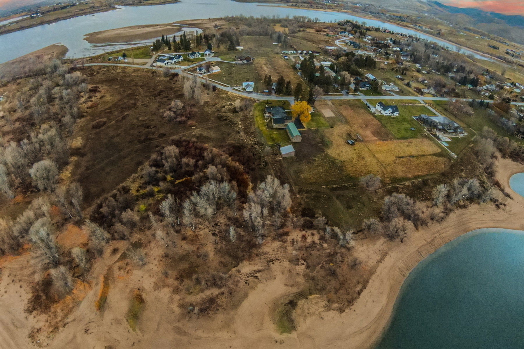 Aerial perspective showcasing a property with waterfront access, surrounded by varied terrain including wooded areas and open land
