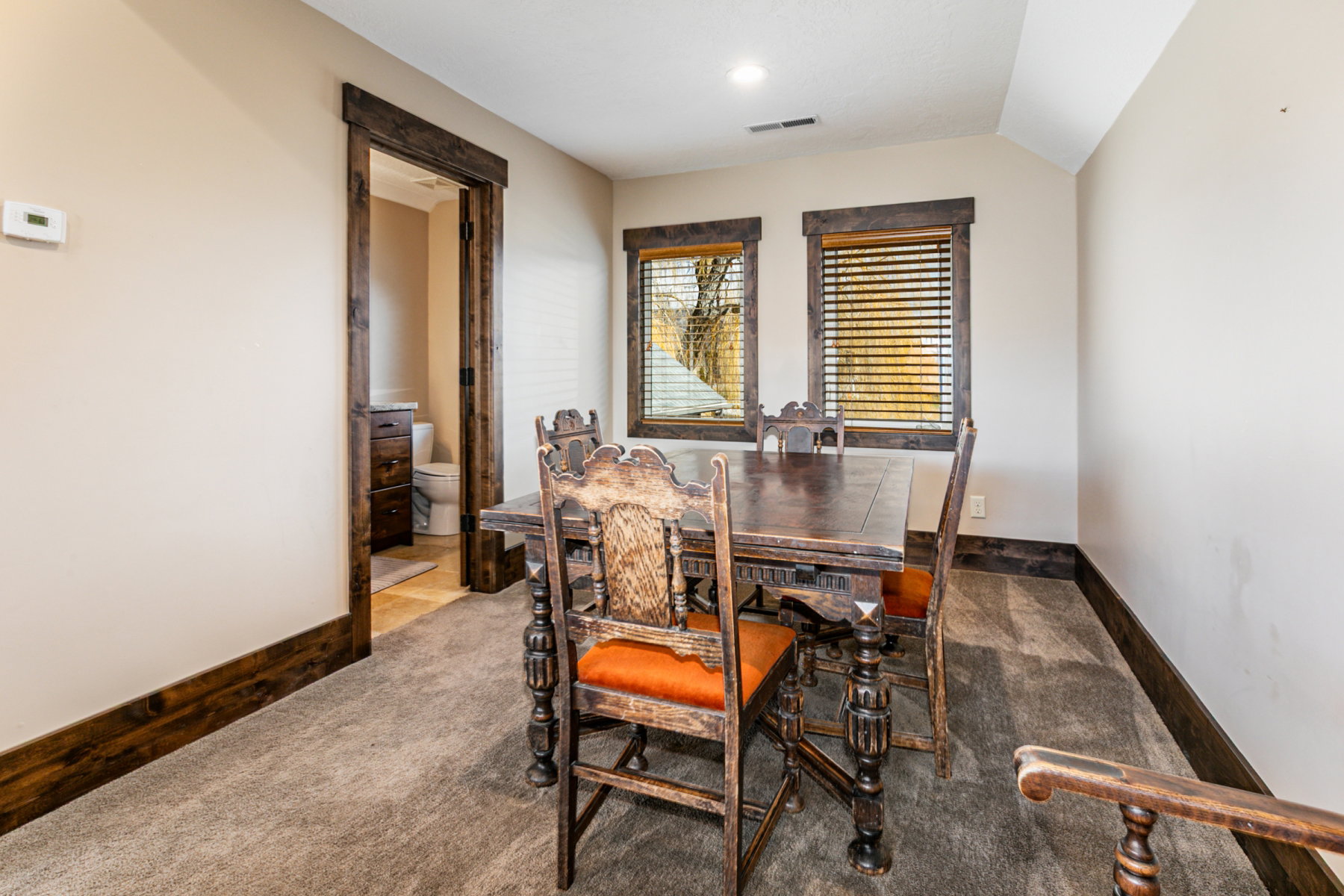 Carpeted room featuring two windows with wood blinds, wood-trimmed doorways, and wood baseboards