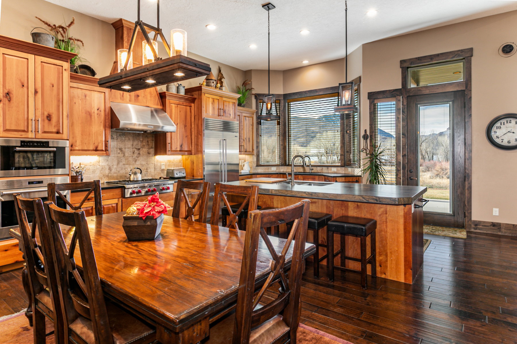 Gourmet kitchen featuring a wood-finish dining table and matching chairs, stainless steel appliances, abundant wood cabinetry, a large kitchen island with bar seating, and dark wood-finish flooring