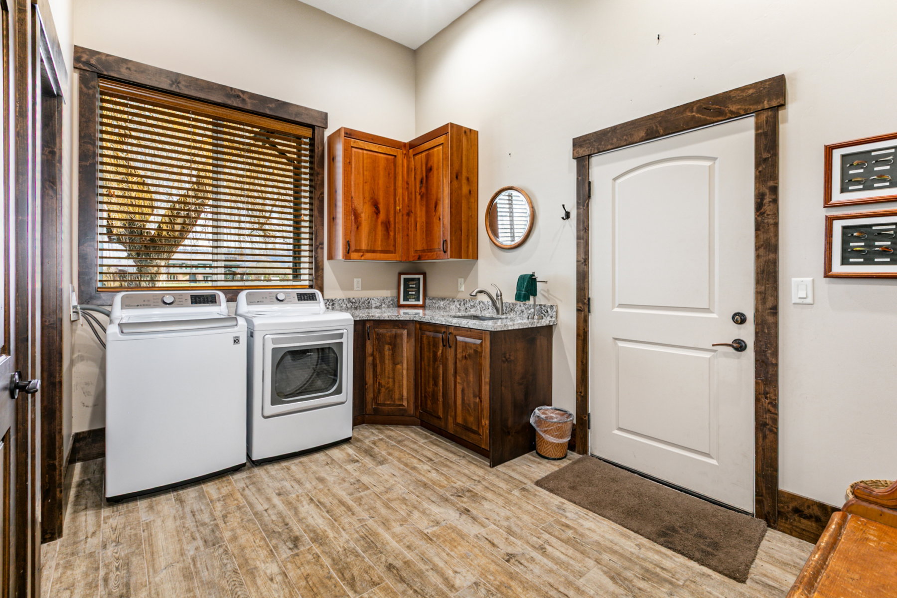 Laundry room featuring wood-finish flooring, corner sink with countertop, upper and lower cabinetry, and a window with blinds