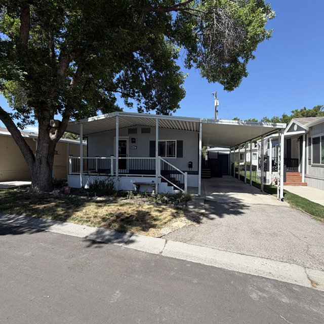 Light gray exterior with a covered front porch, white railing, dark shutters  & covered parking space.