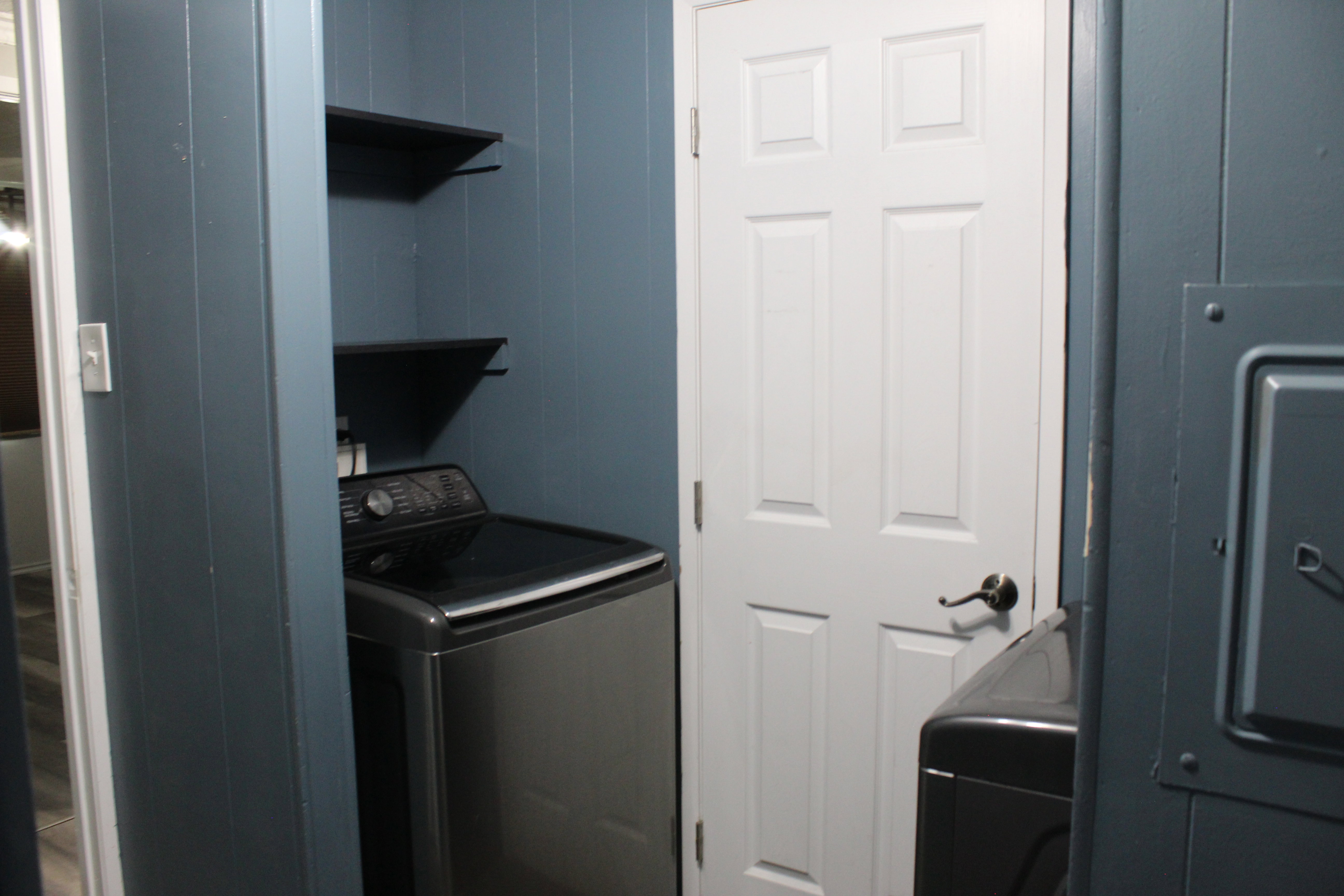 Dedicated laundry area featuring a top-loading appliance, wall-mounted shelving, and paneled walls