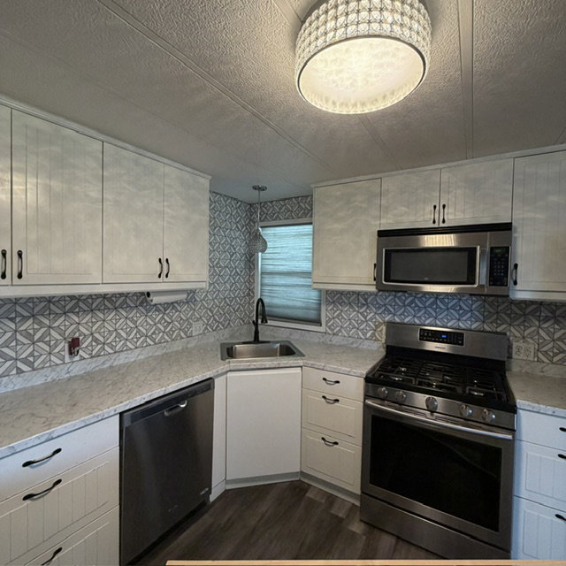 Upclose view of the kitchen.Updated kitchen featuring white cabinetry, stainless steel appliances, patterned tile backsplash, light-toned countertops, and wood-finish flooring