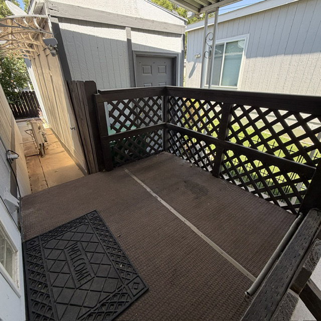Outdoor patio space featuring a brown lattice railing and a brown textured floor. At the end of the driveway.